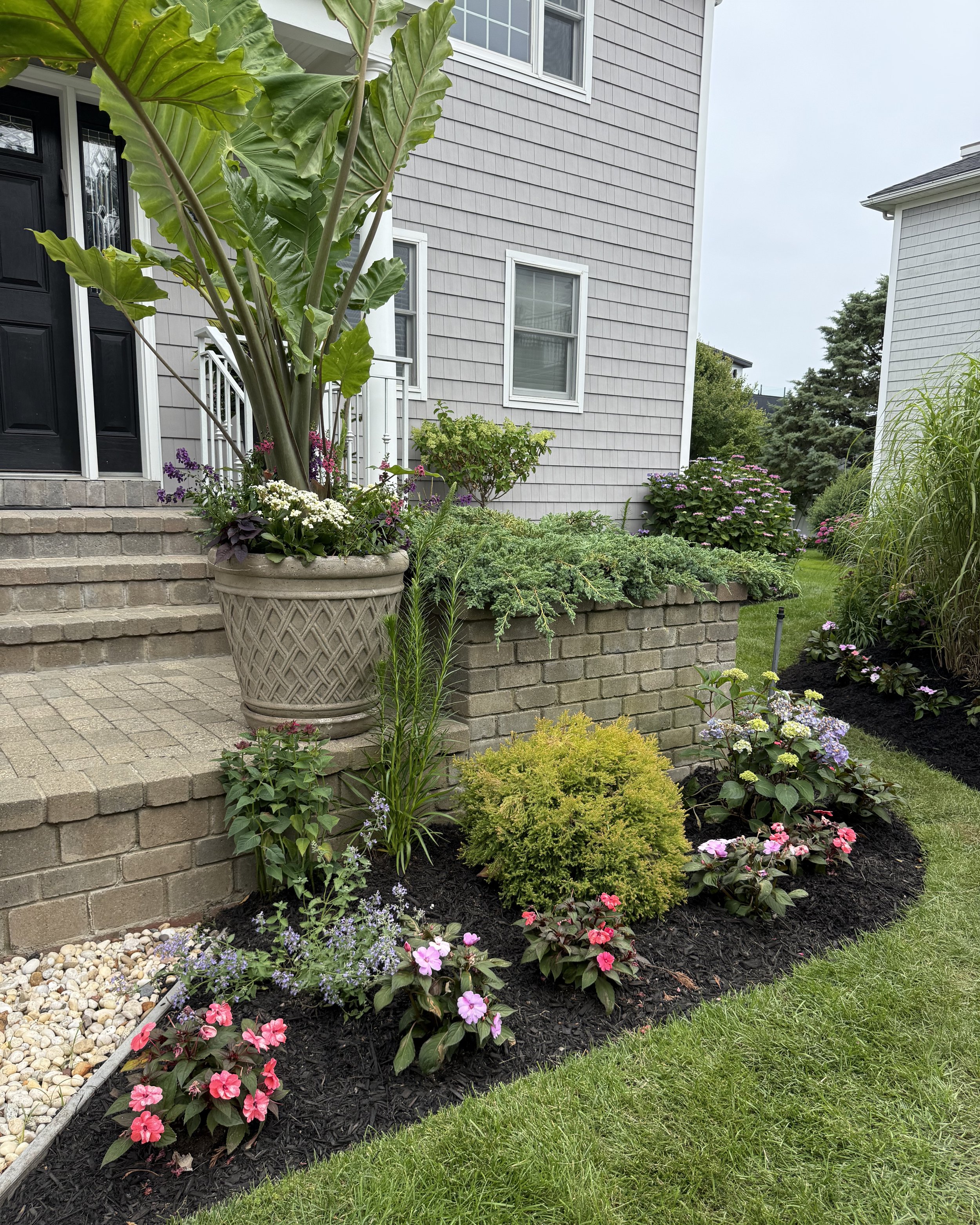 Manicured foundation planting with impatiens and mixed flowers in custom planter pot — landscape design by Chasky, Atlantic Beach NY