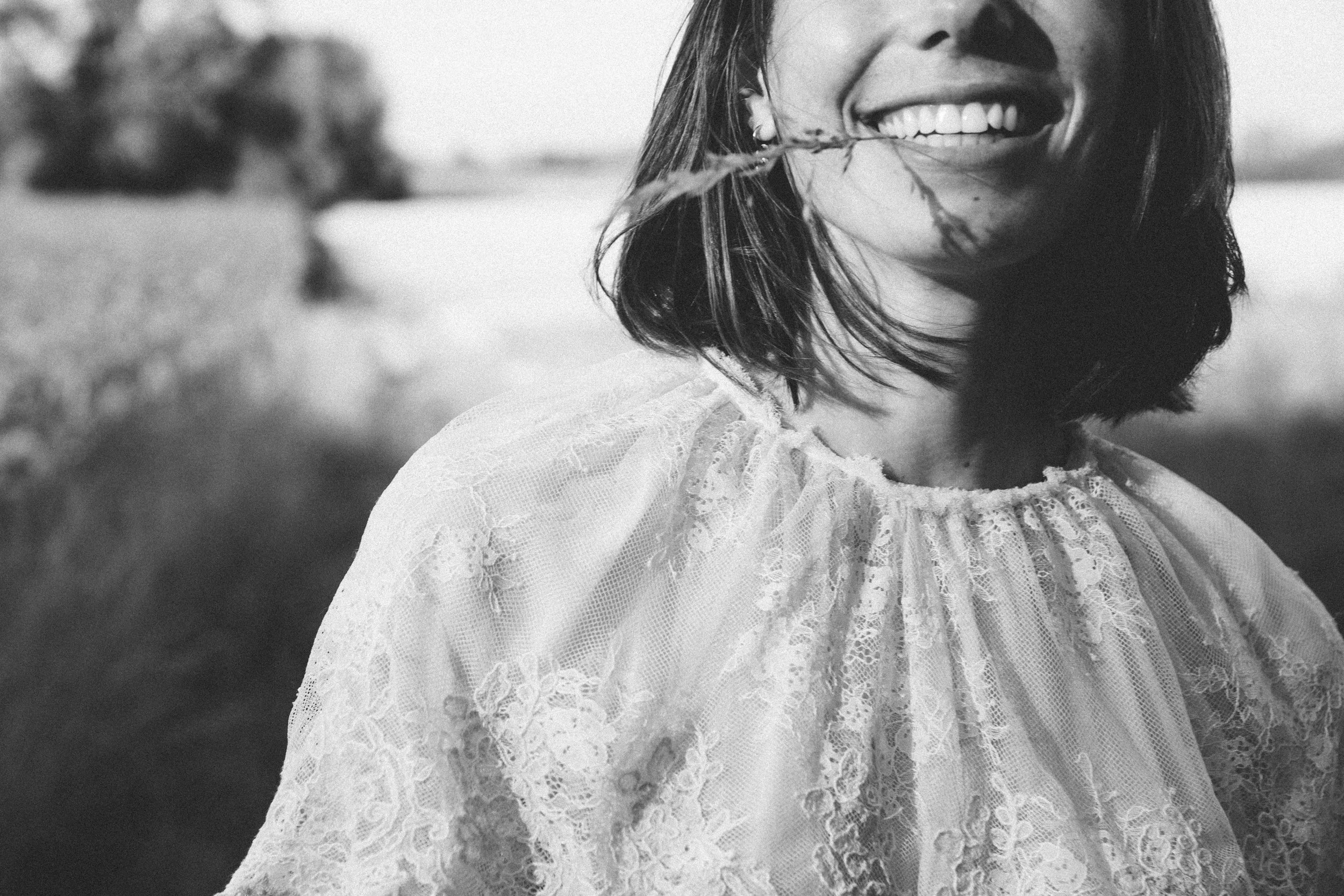 Close-up of a woman smiling, with a partial view of her face, hair, and a lace dress in black and white.