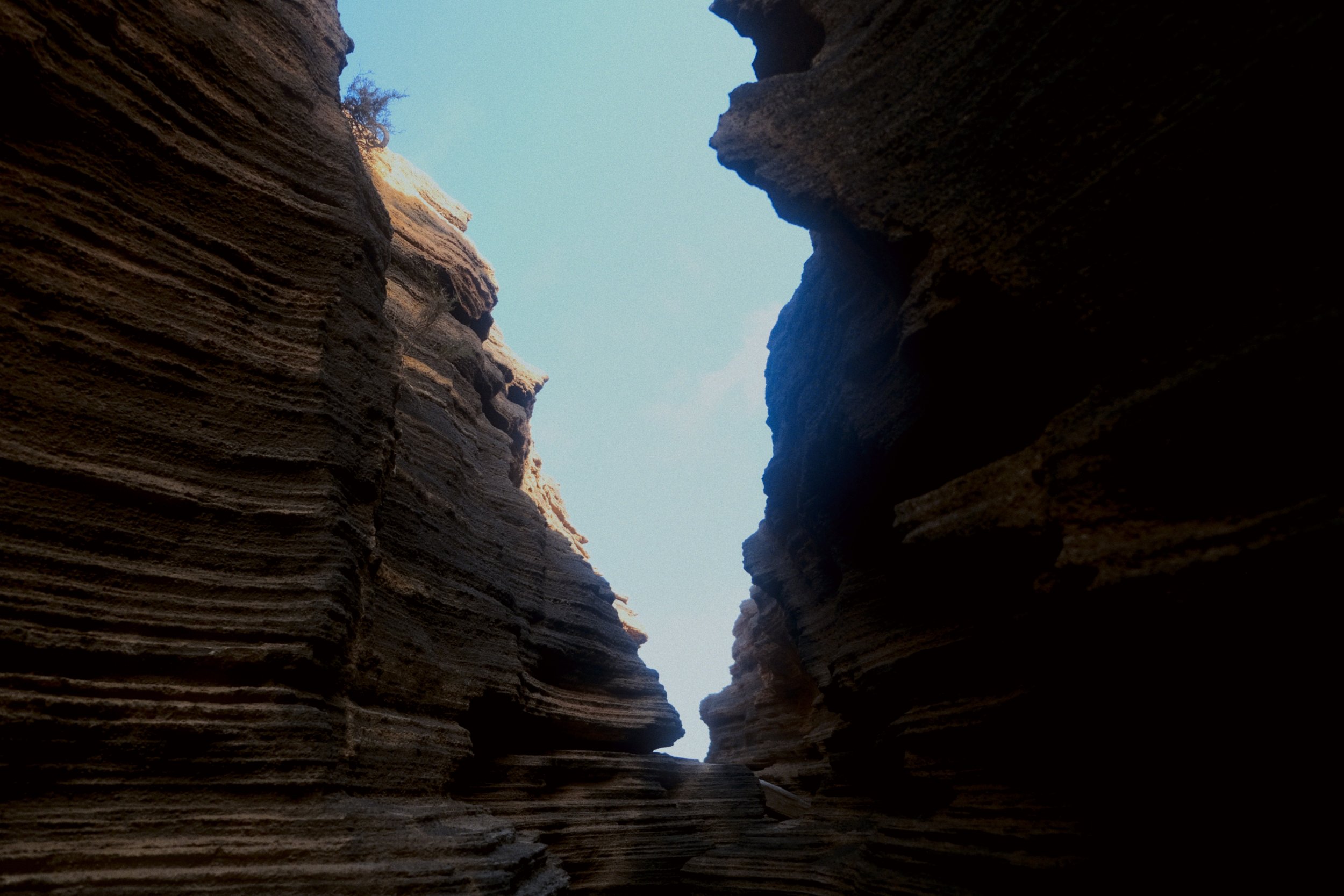 Une vue depuis le fond d'une gorge ou d'une crevasse avec des parois rocheuses verticales, laissant apparaître le ciel bleu au-dessus.