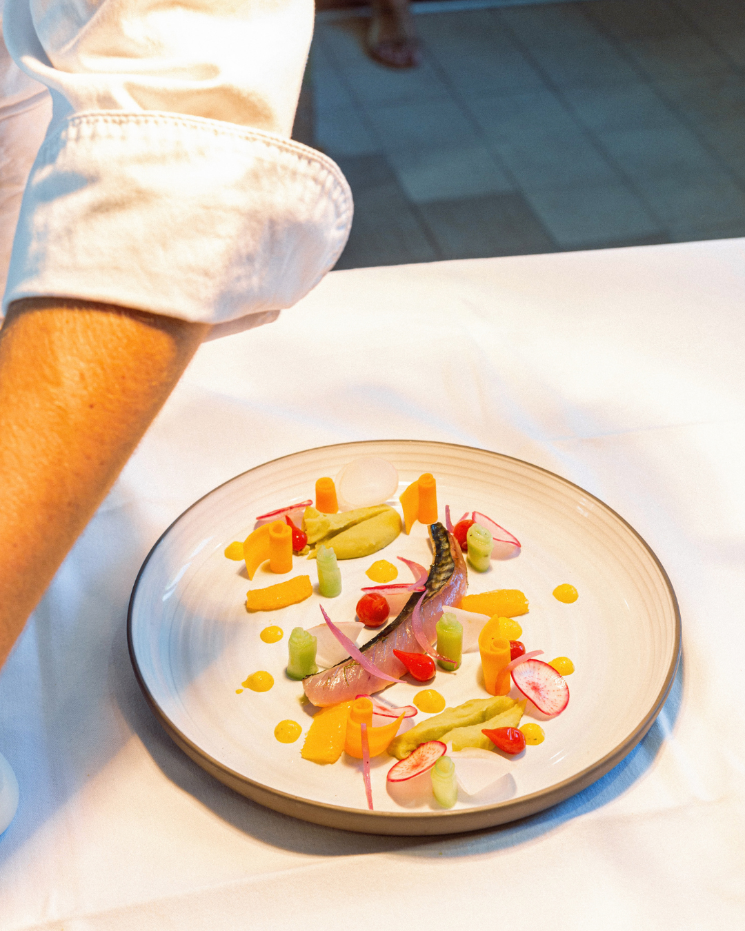 Assiette de poisson accompagné de légumes et de sauces colorées, présentée de manière artistique.