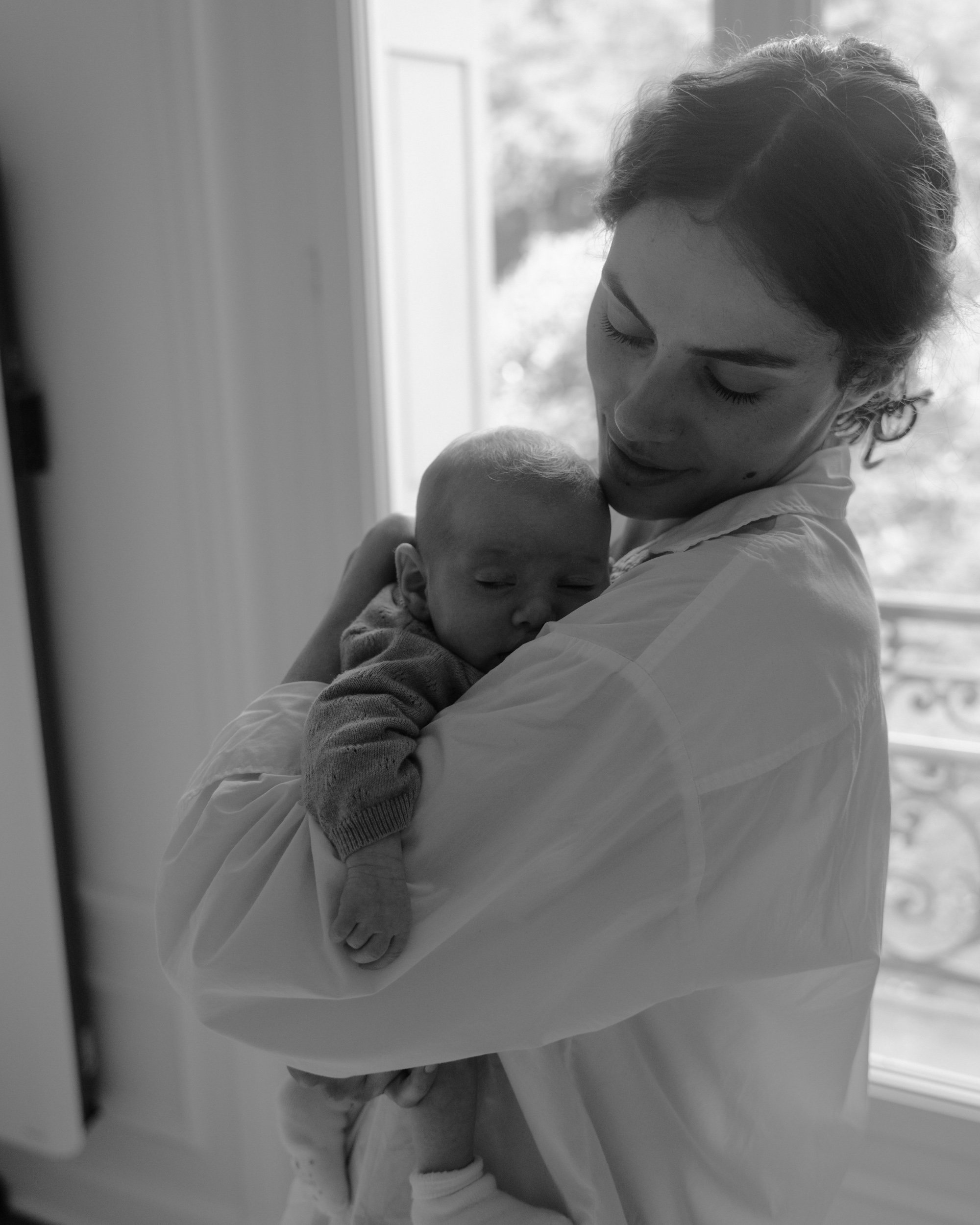 Une femme tient un bébé dans ses bras, dans un intérieur lumineux.