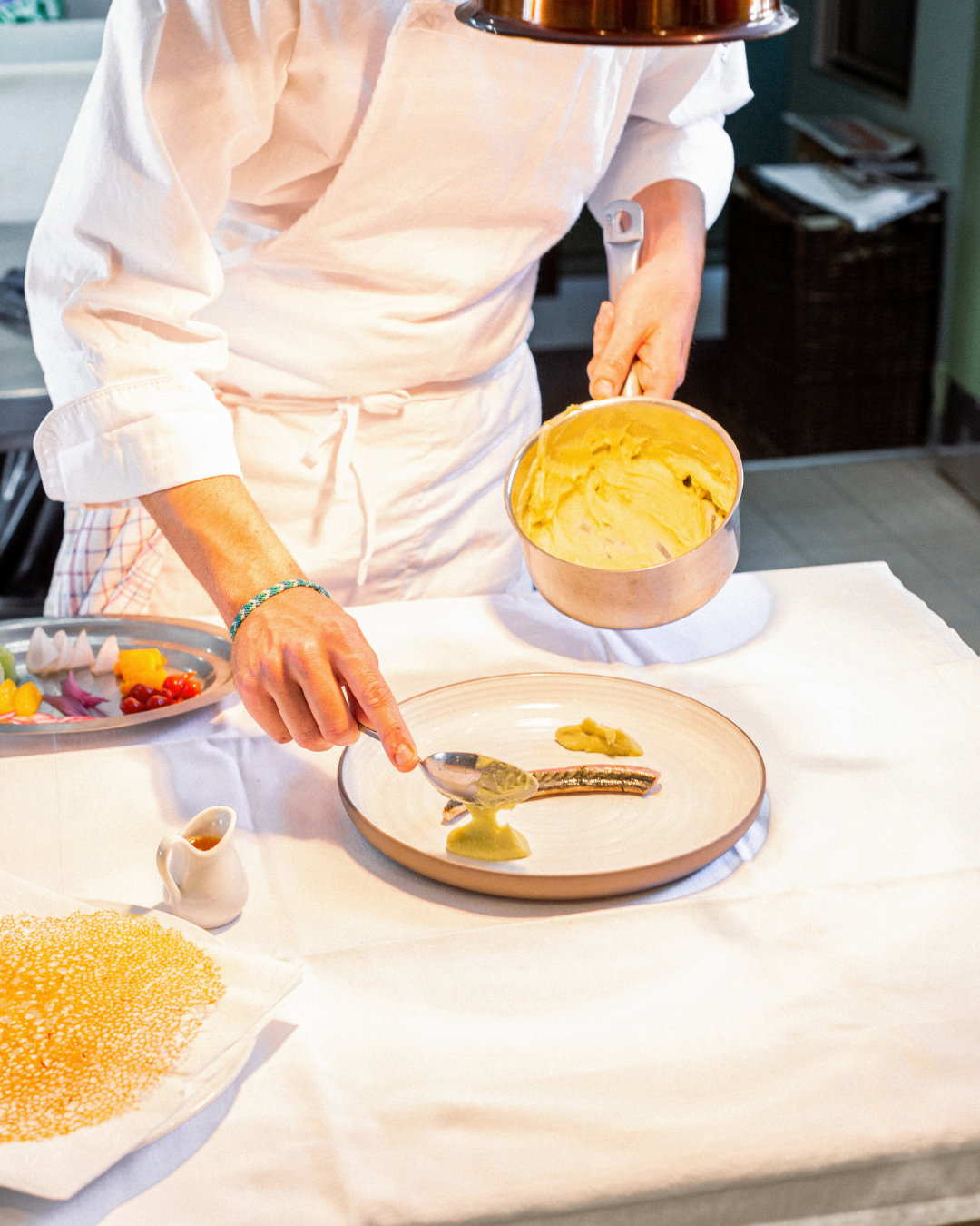 Un chef en train de dresser une assiette en déposant de la purée sur un plat