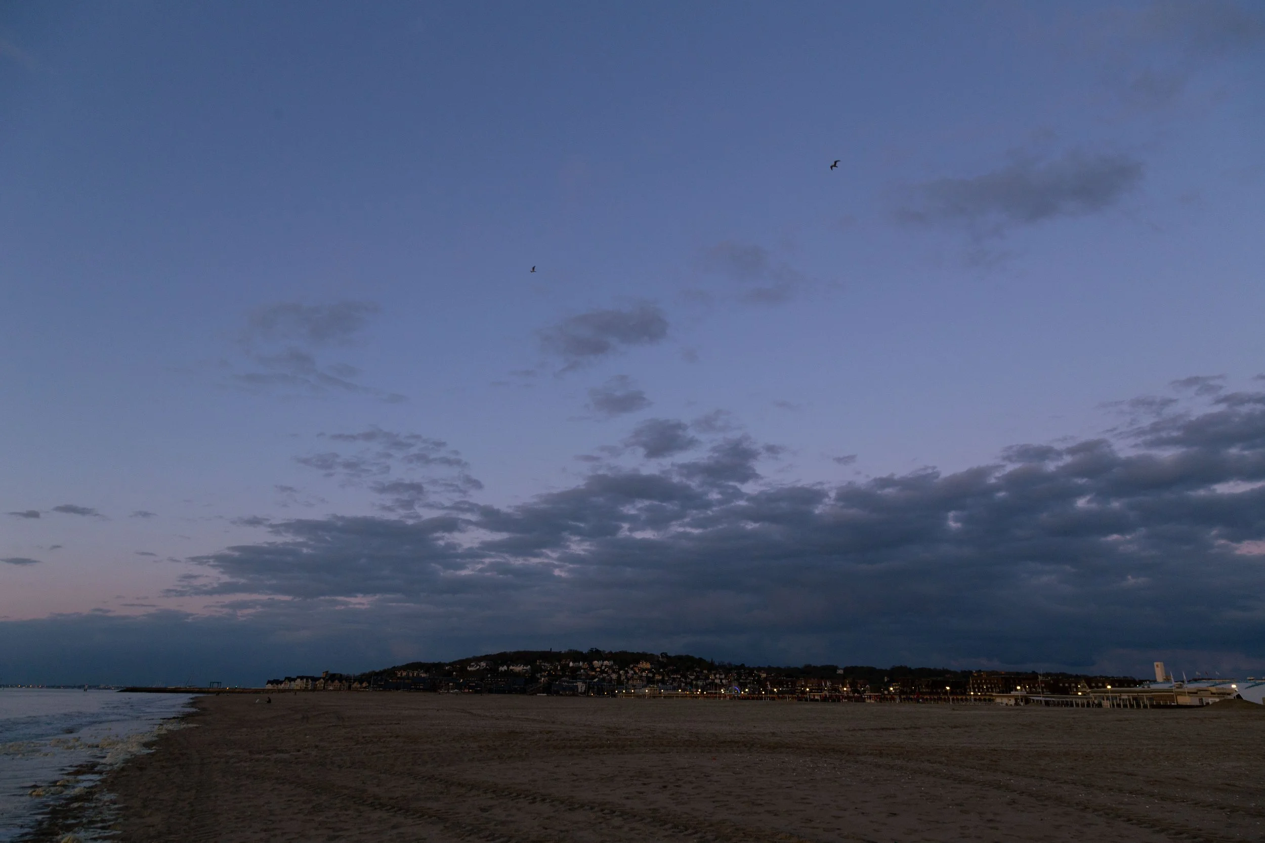 Coucher ou lever de soleil sur une plage avec des nuages dans le ciel et des oiseaux volant, vue d'une ville en contrebas.