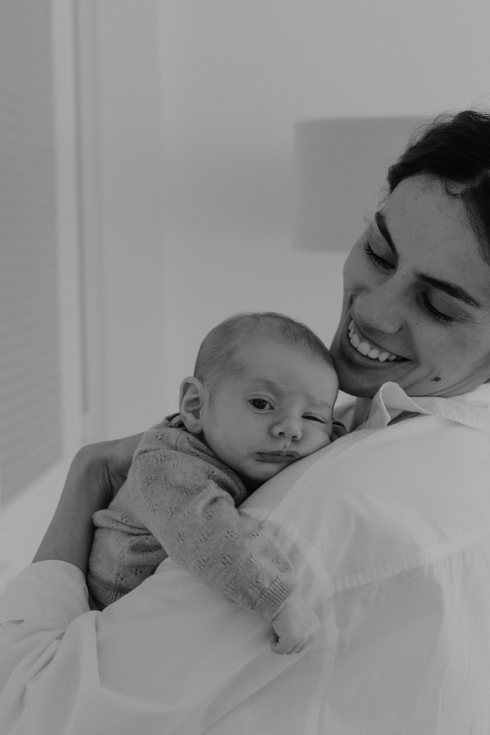 Une femme souriante tient un jeune enfant dans ses bras, dans une ambiance chaleureuse et affectueuse.