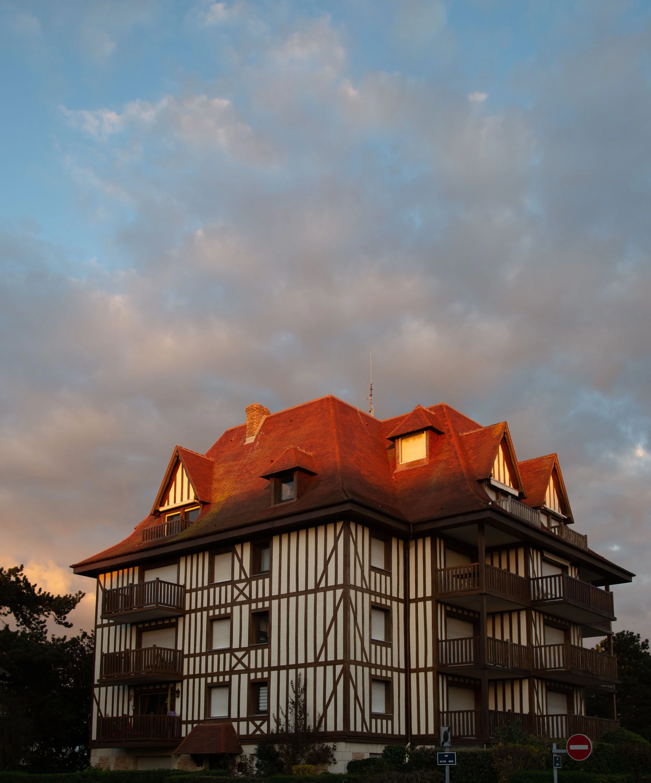 Immeuble résidentiel de style toscan avec façade en bois et balcons en bois, sous un ciel nuageux au coucher du soleil.
