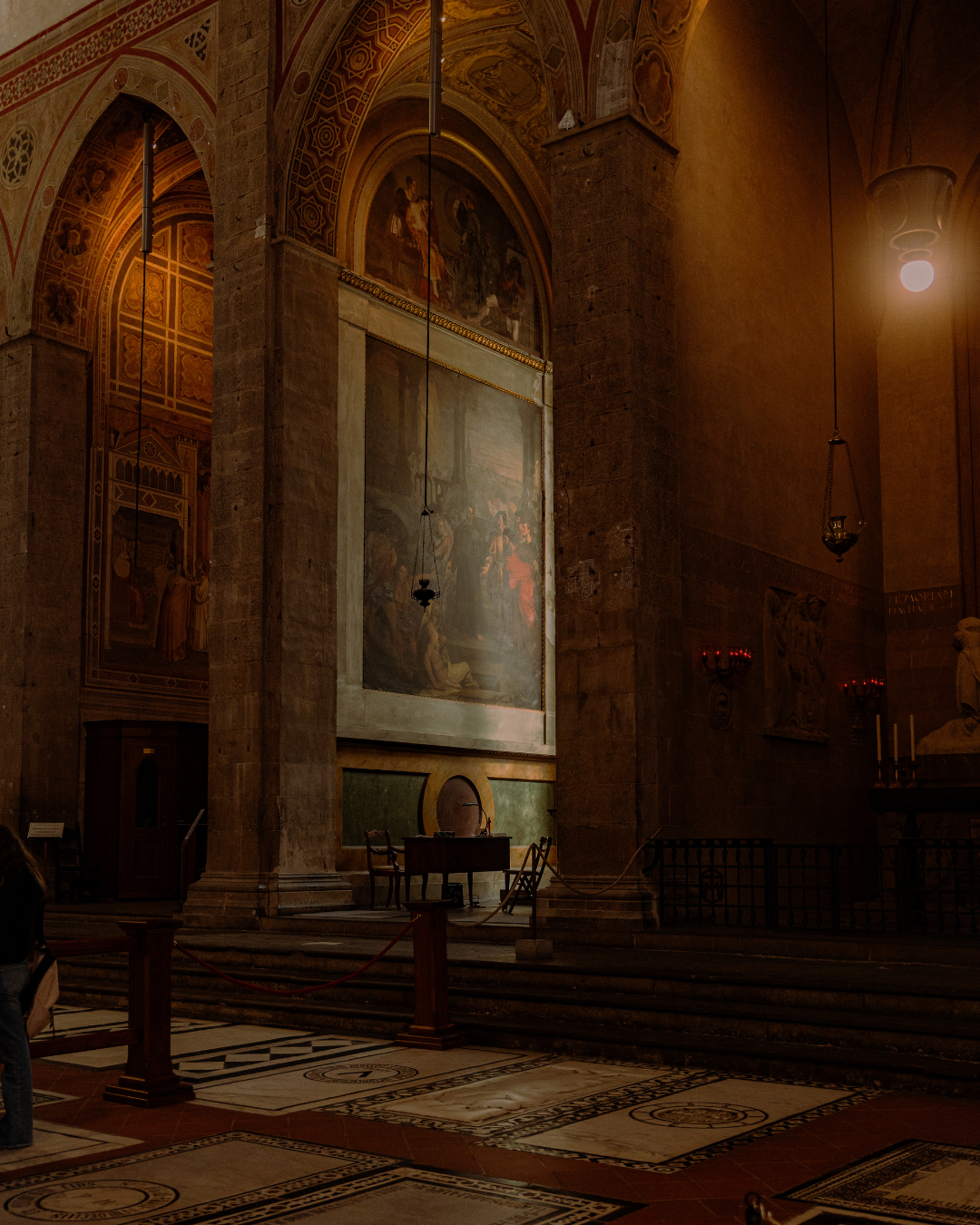 Intérieur d'une église avec de grandes fresques murales, chandeliers suspendus et un espace de prière avec des chaises et un autel.