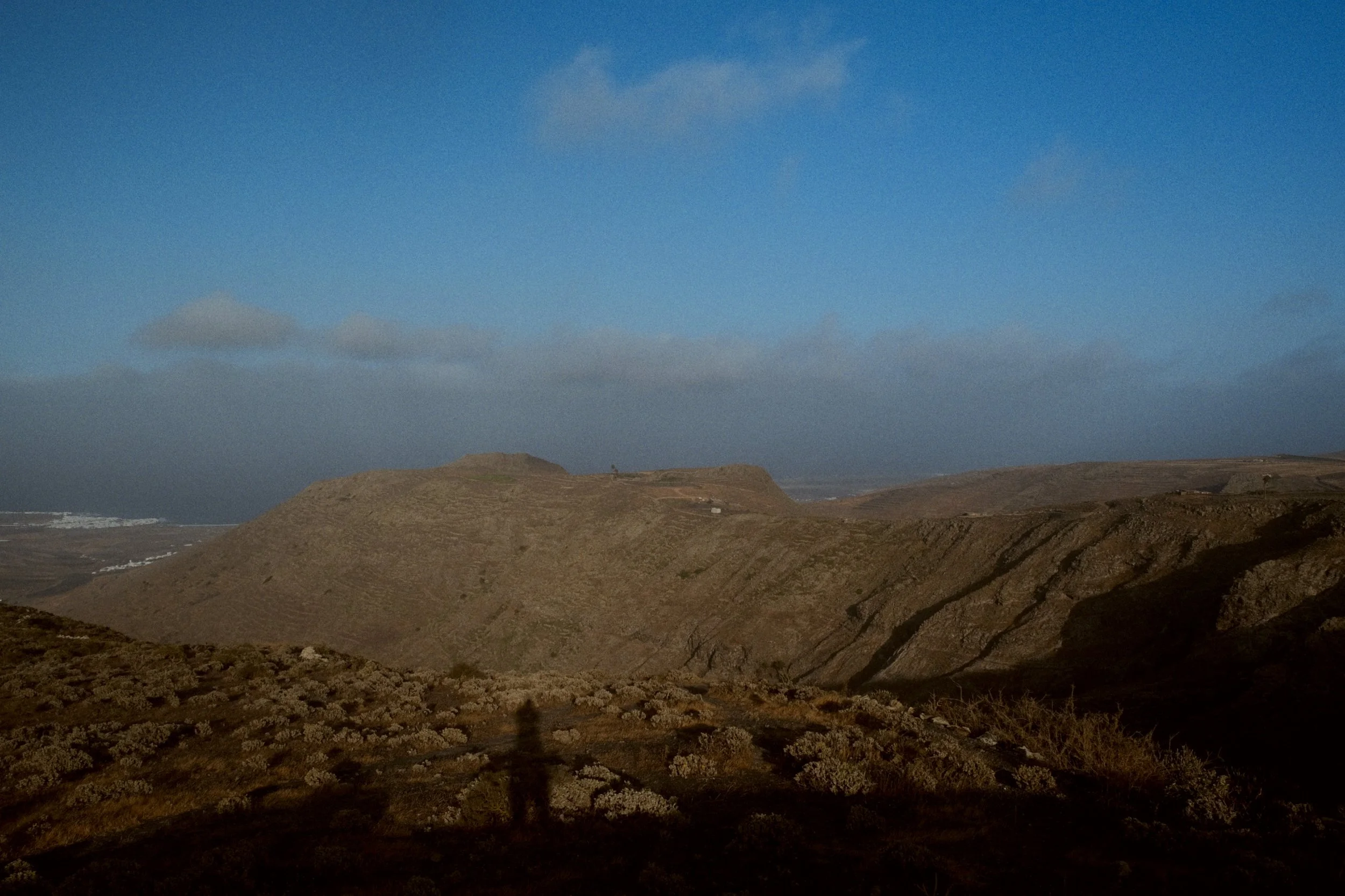 Paysage de collines arides sous un ciel bleu avec quelques nuages.