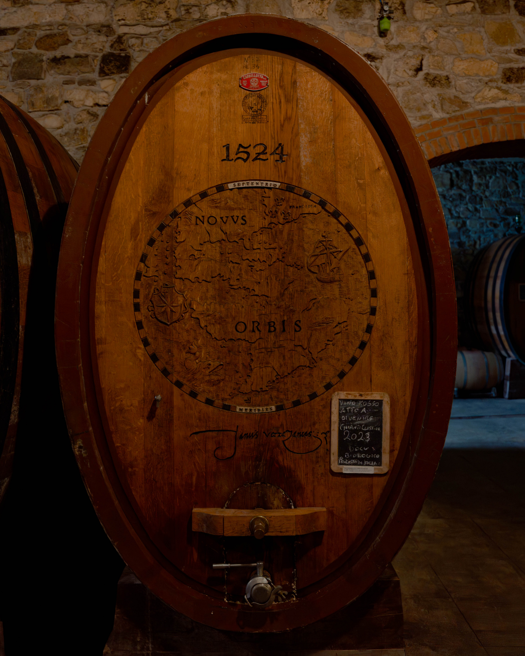 Fût de vin en bois avec une carte gravée représentant une carte du monde et la date 1524, dans une cave à vin en pierre et en brique.