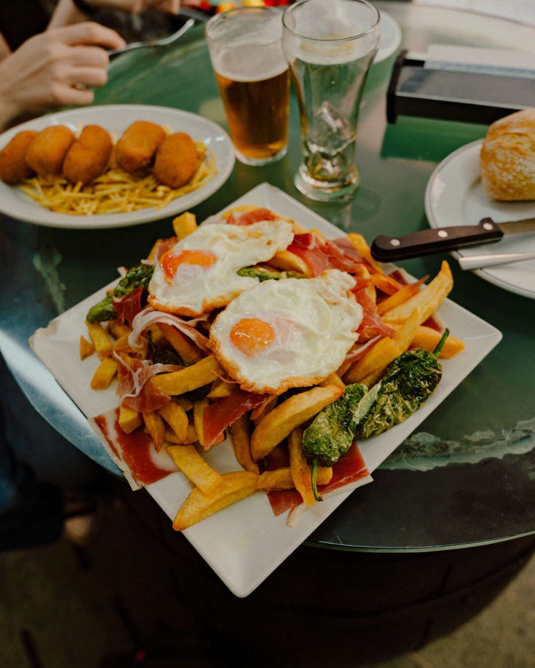 Plat de frites avec œufs au plat, jambon, poivrons verts, et burrata. Inclut aussi des croquettes frites et des boissons.