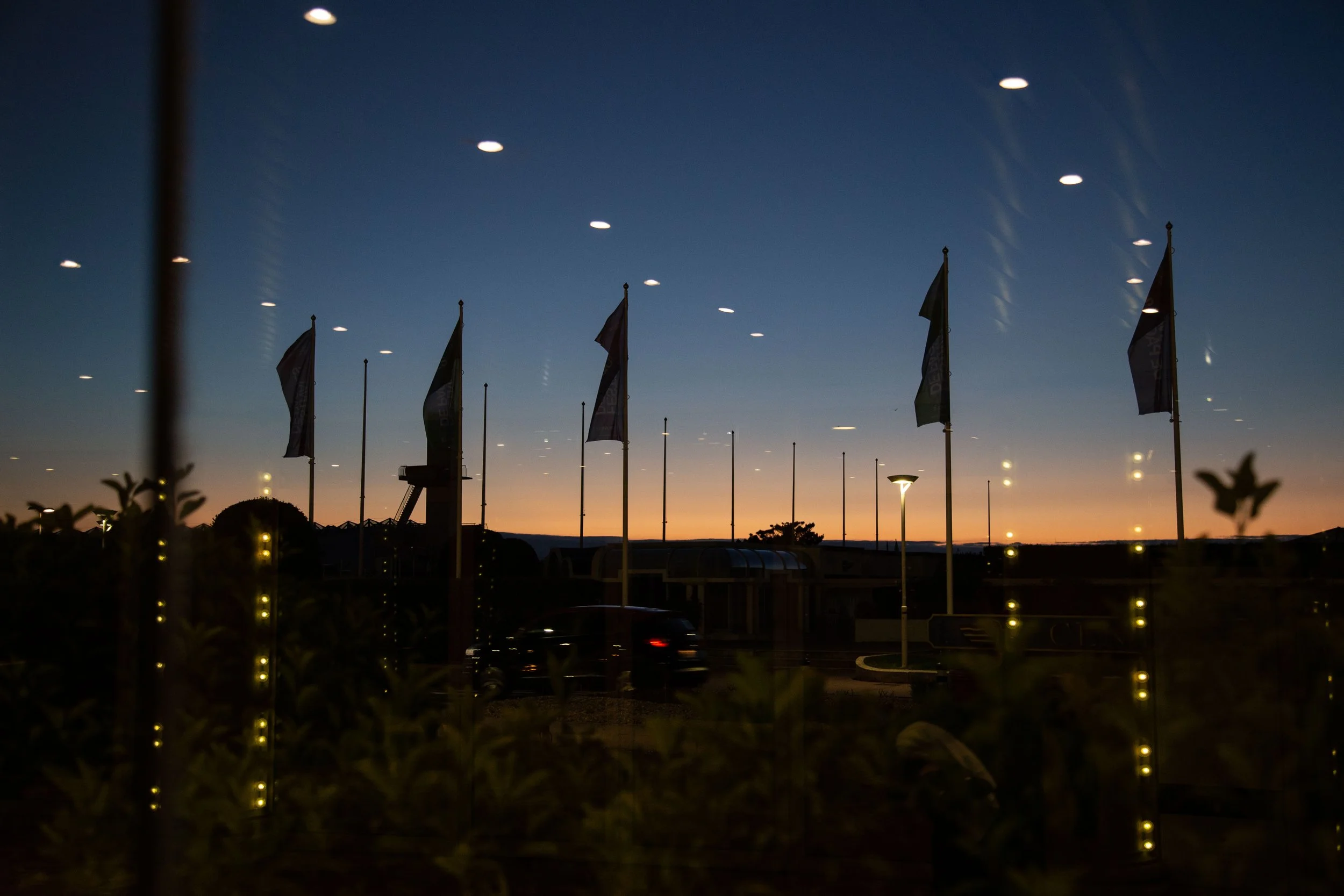 Coucher de soleil avec drapeaux et lampadaires éclairés dans un parc ou un espace public.