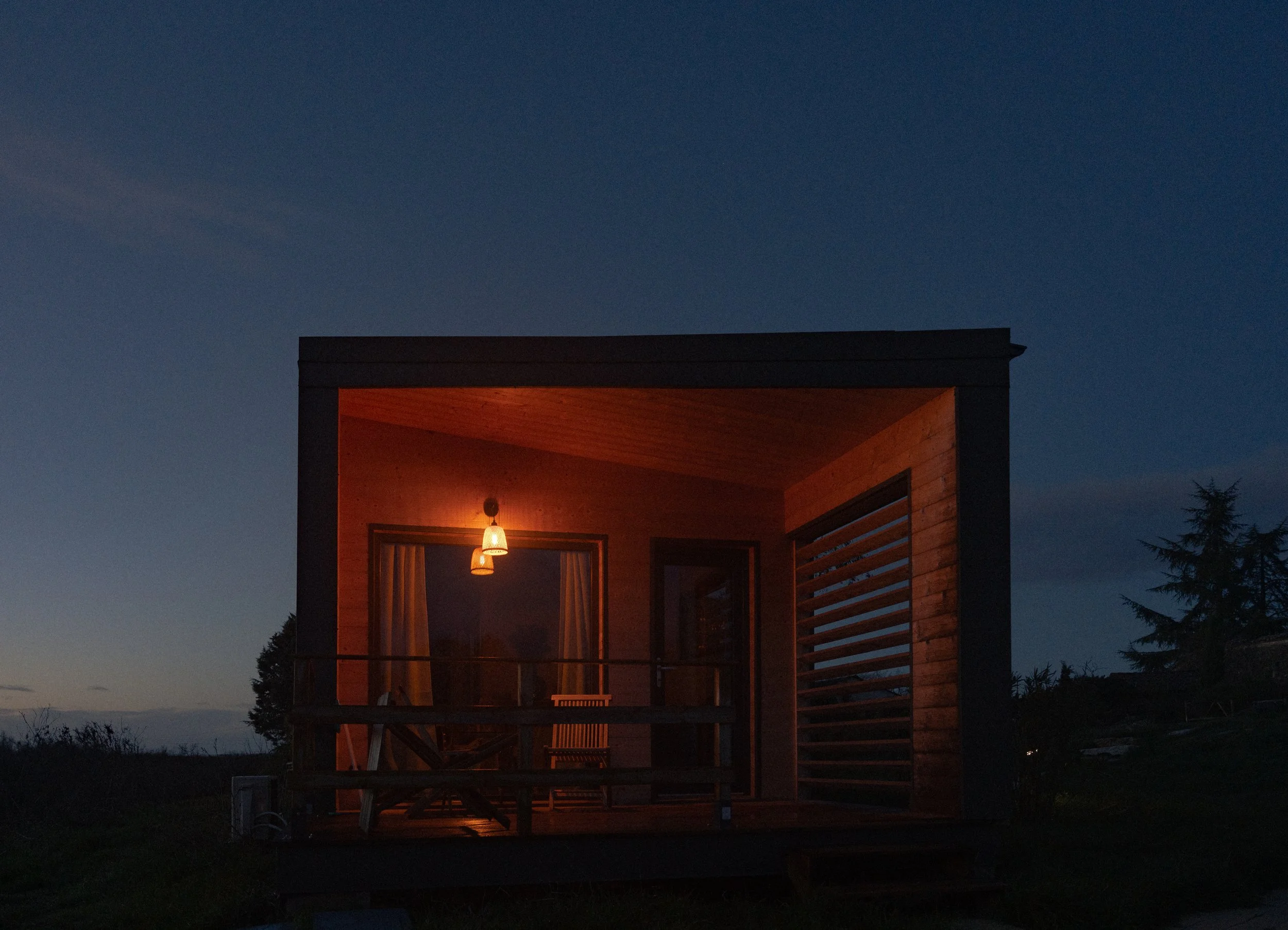 Une cabane en bois illuminée la nuit, située en plein air avec un ciel étoilé en arrière-plan.