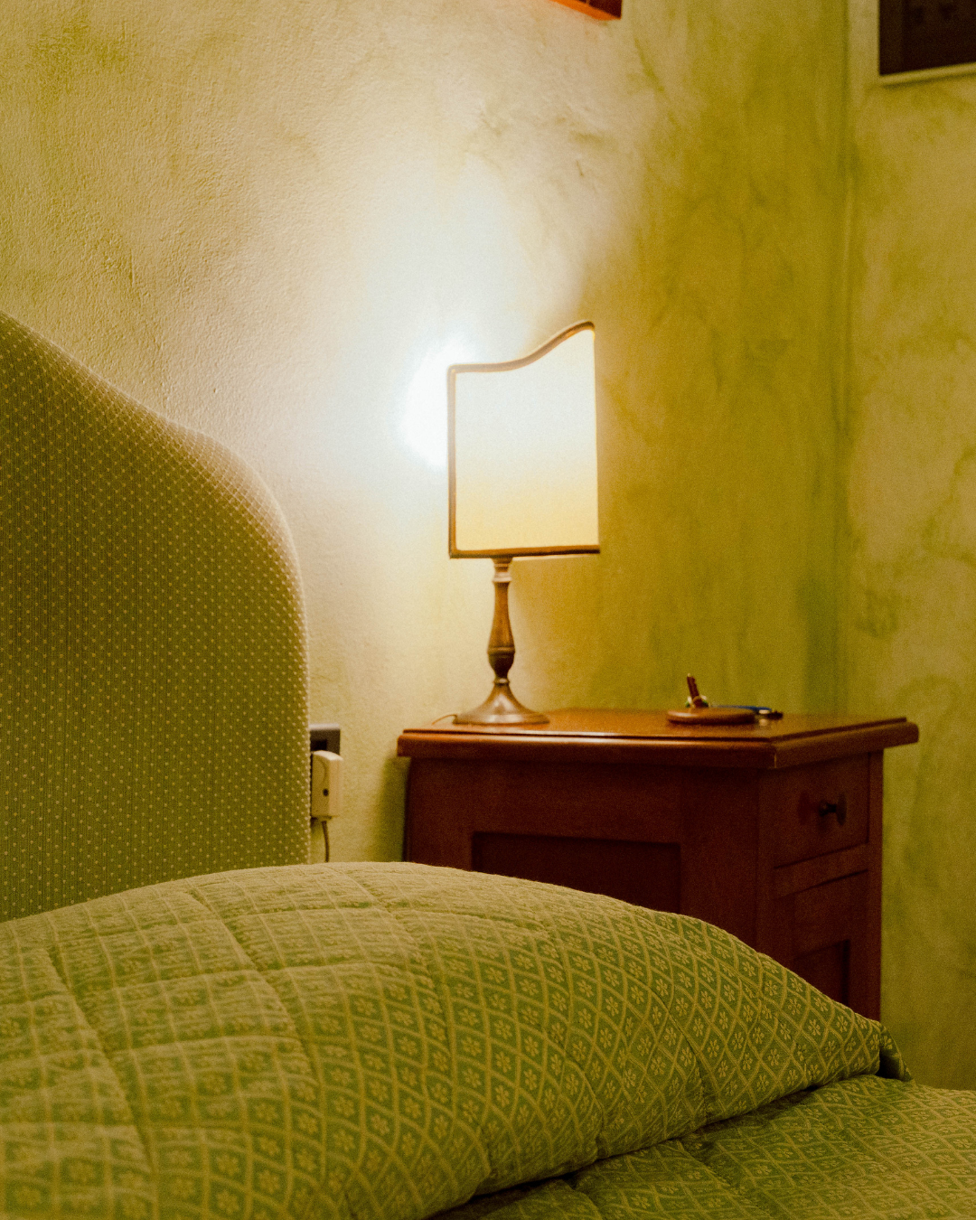 Couch en tissu vert avec coussin, lampe de chevet en bois avec abat-jour beige, mur crème dans une chambre.