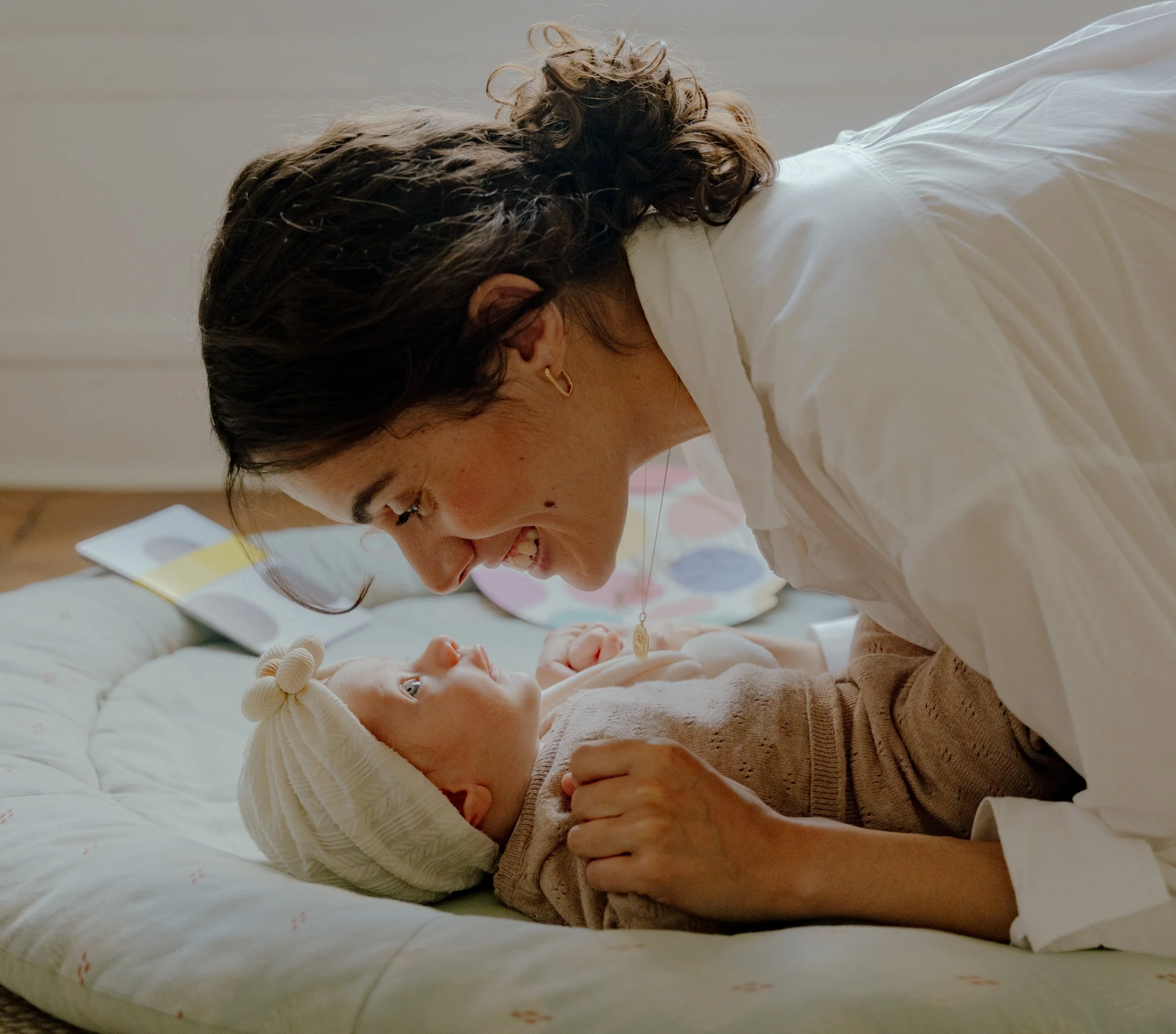 Une femme et un bébé partageant un moment de tendresse sur un lit, la femme souriant tendrement vers le bébé.
