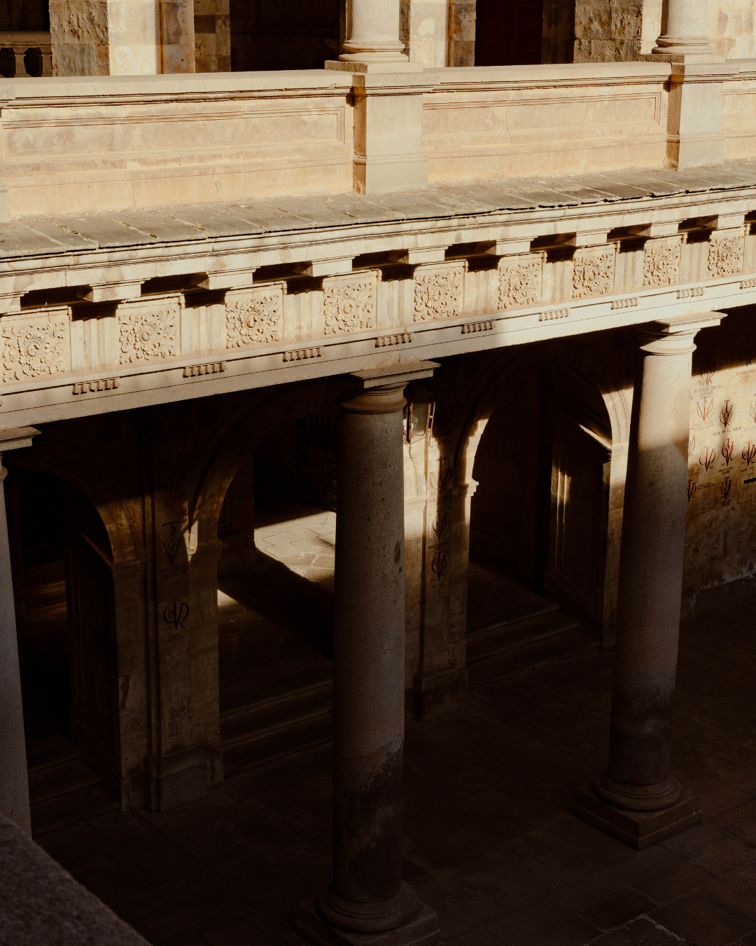 Une vue de colonnes en pierre et d'une balustrade ornée à l'étage dans un bâtiment historique, avec une lumière dorée
