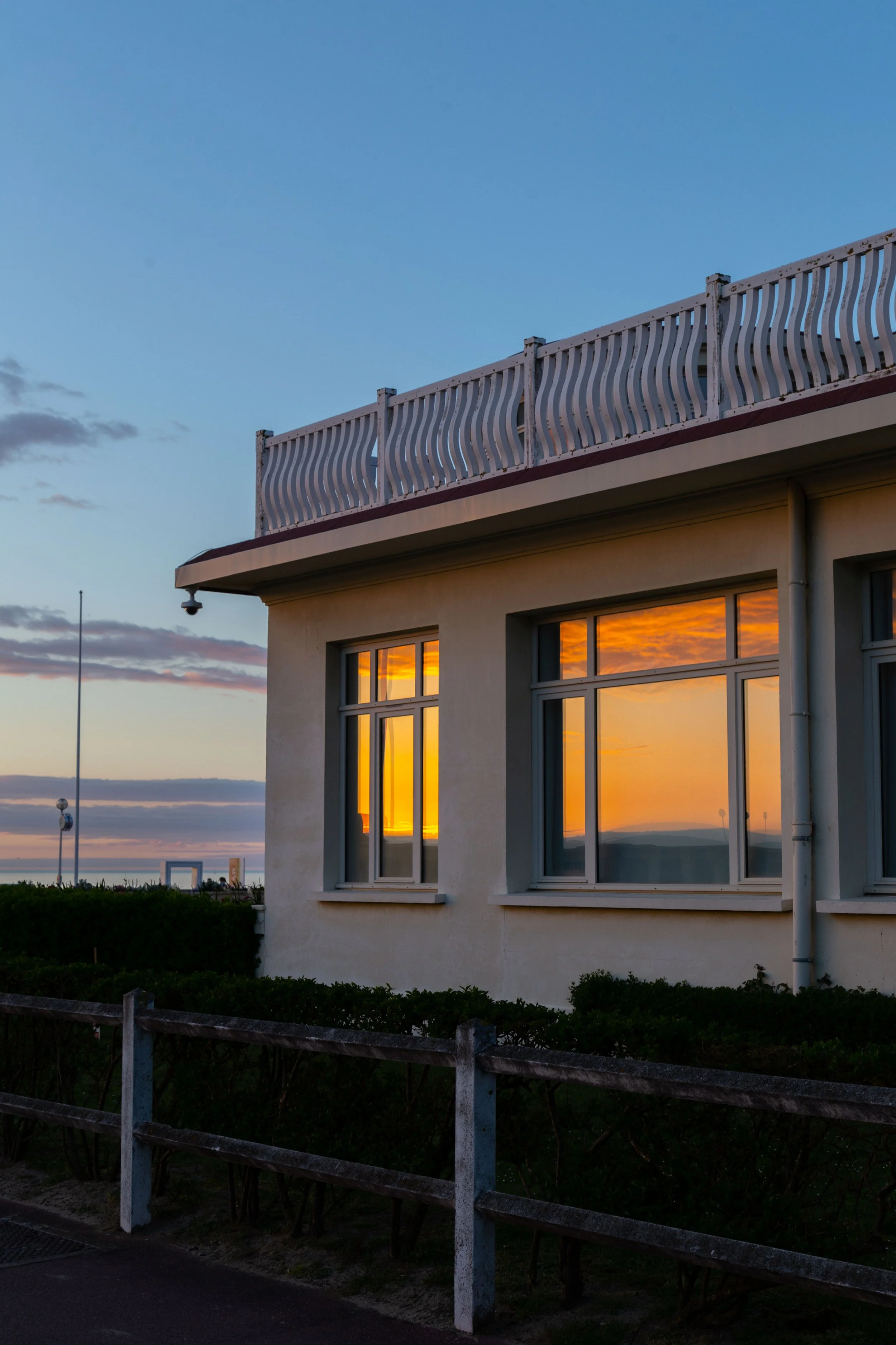 Bâtiment avec fenêtres illuminées par un coucher de soleil, railing blanc sur le balcon, ciel bleu avec quelques nuages