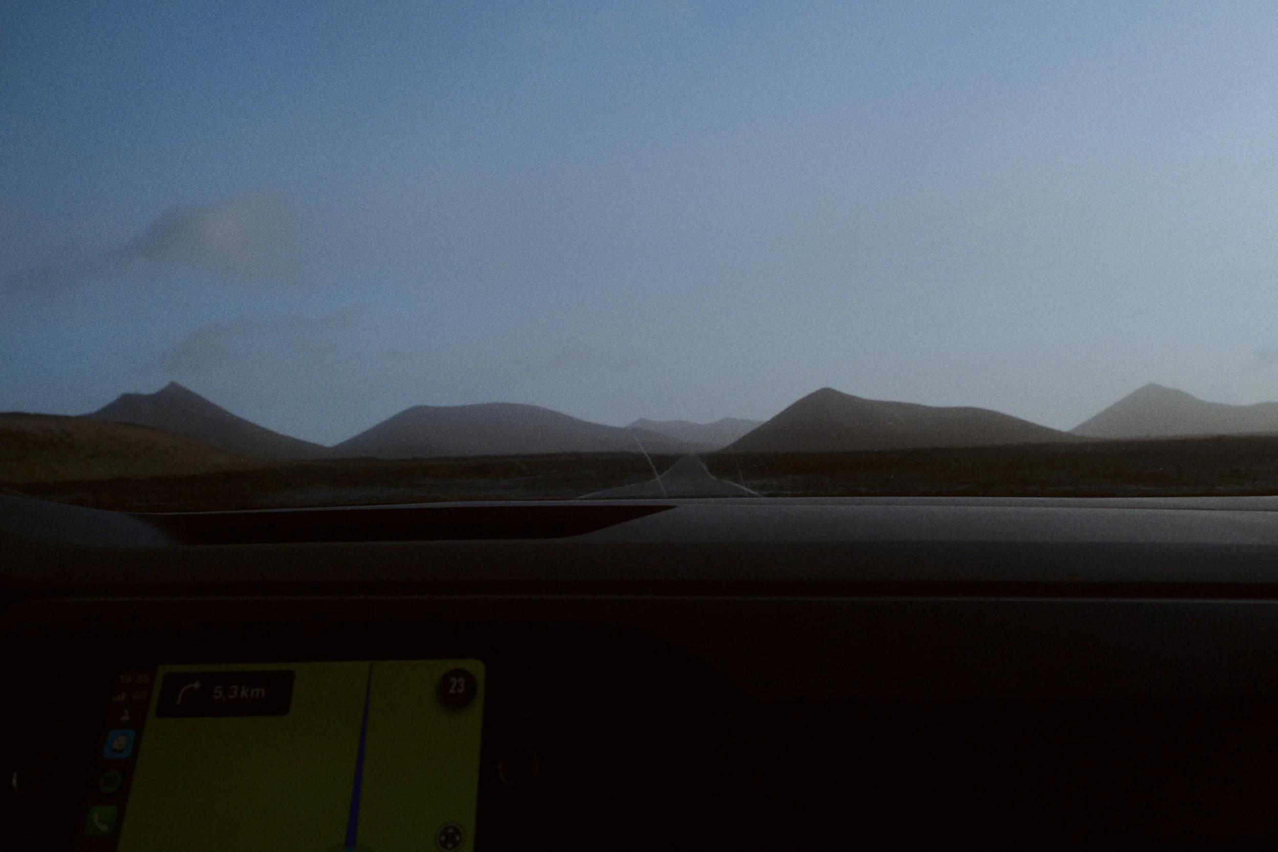 Vue depuis l'intérieur d'une voiture montrant un paysage de montagnes sous un ciel clair, avec un GPS affichant une distance de 5,3 km. La scène est capturée de l'avant du véhicule, probablement lors d'un voyage en excursion ou en route.