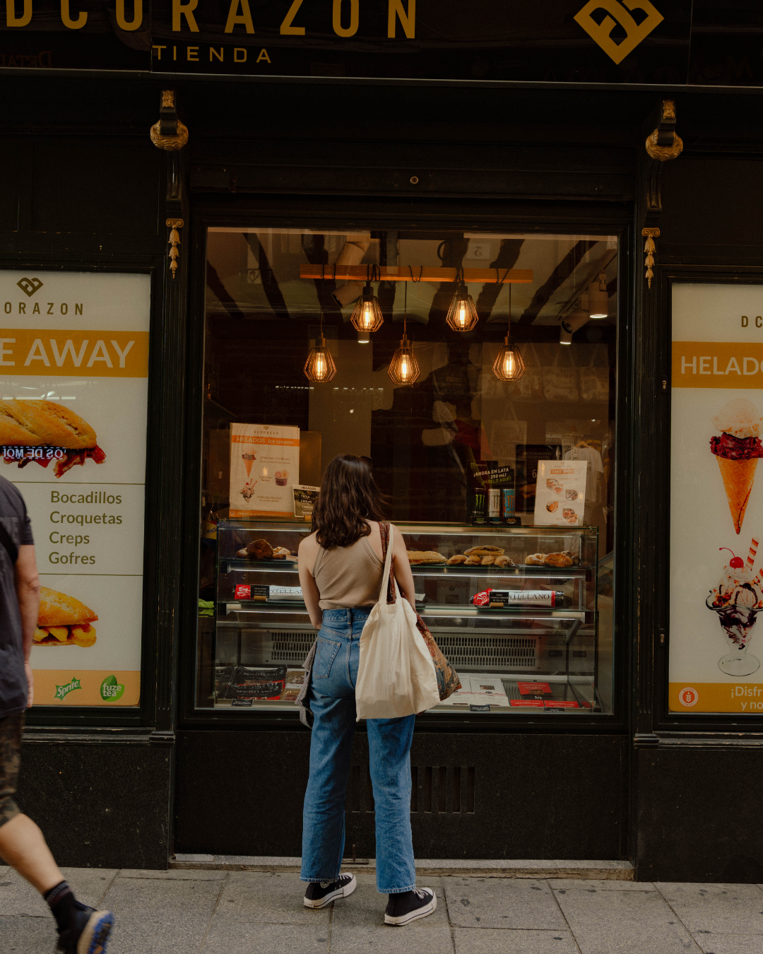 Femme regardant la vitrine d'une boutique de glaces ou de snacks, avec panneau publicitaire à gauche et à droite.