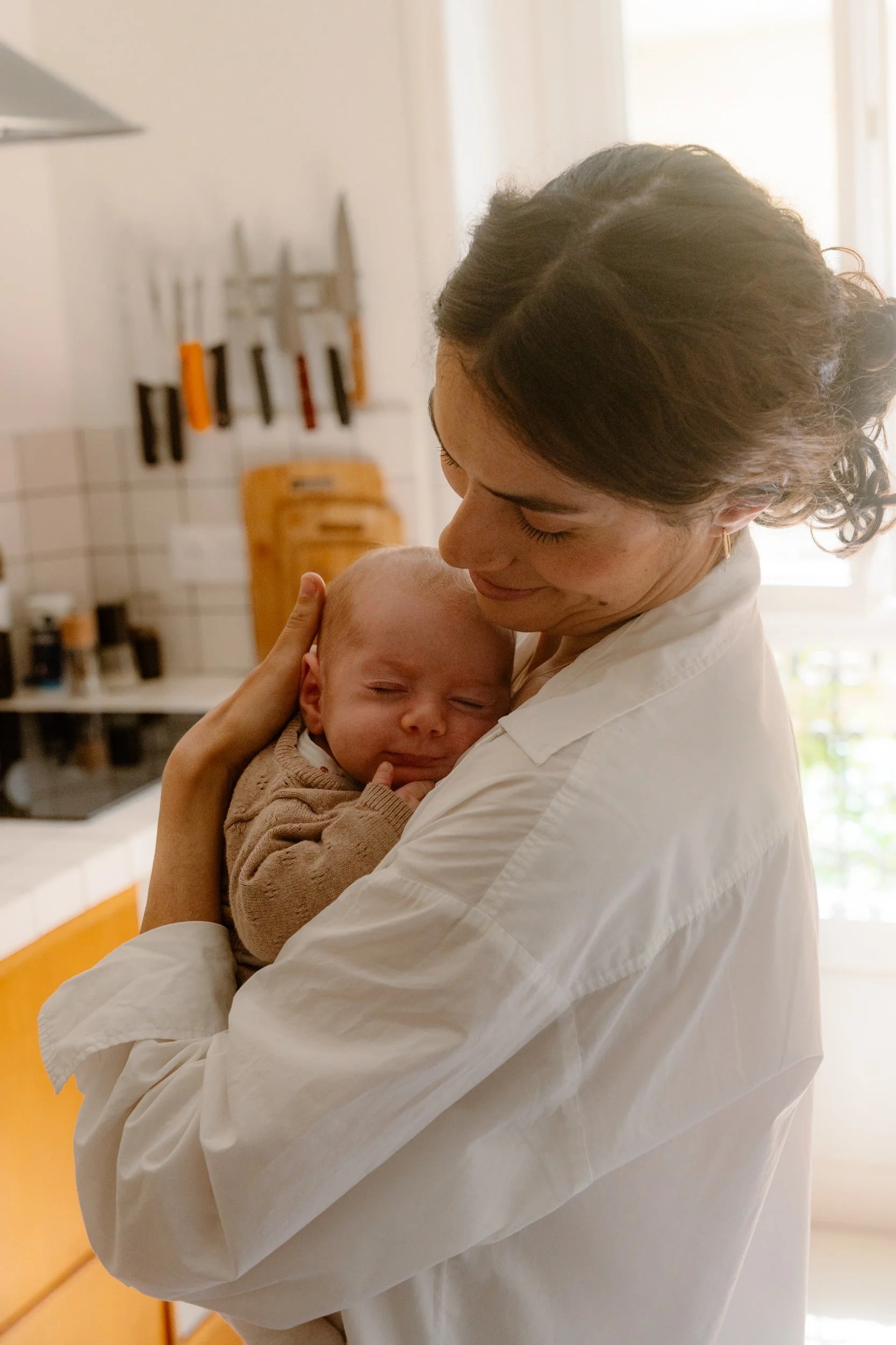 Une femme souriante tient un bébé dans ses bras dans une cuisine lumineuse.