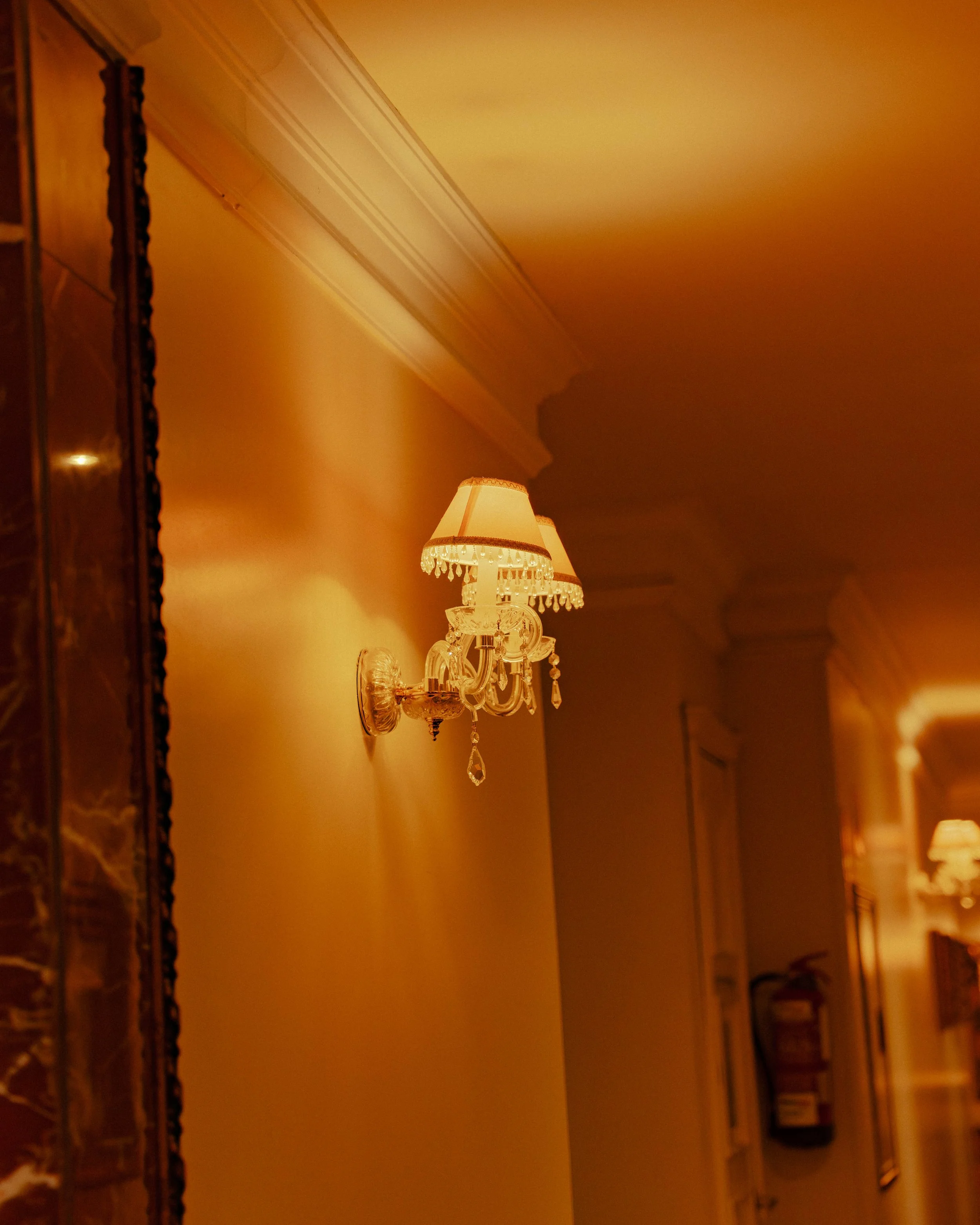 Un mur avec une applique de lampe ornée de cristaux et un luminaire en verre, ambiance chaleureuse, style classique.