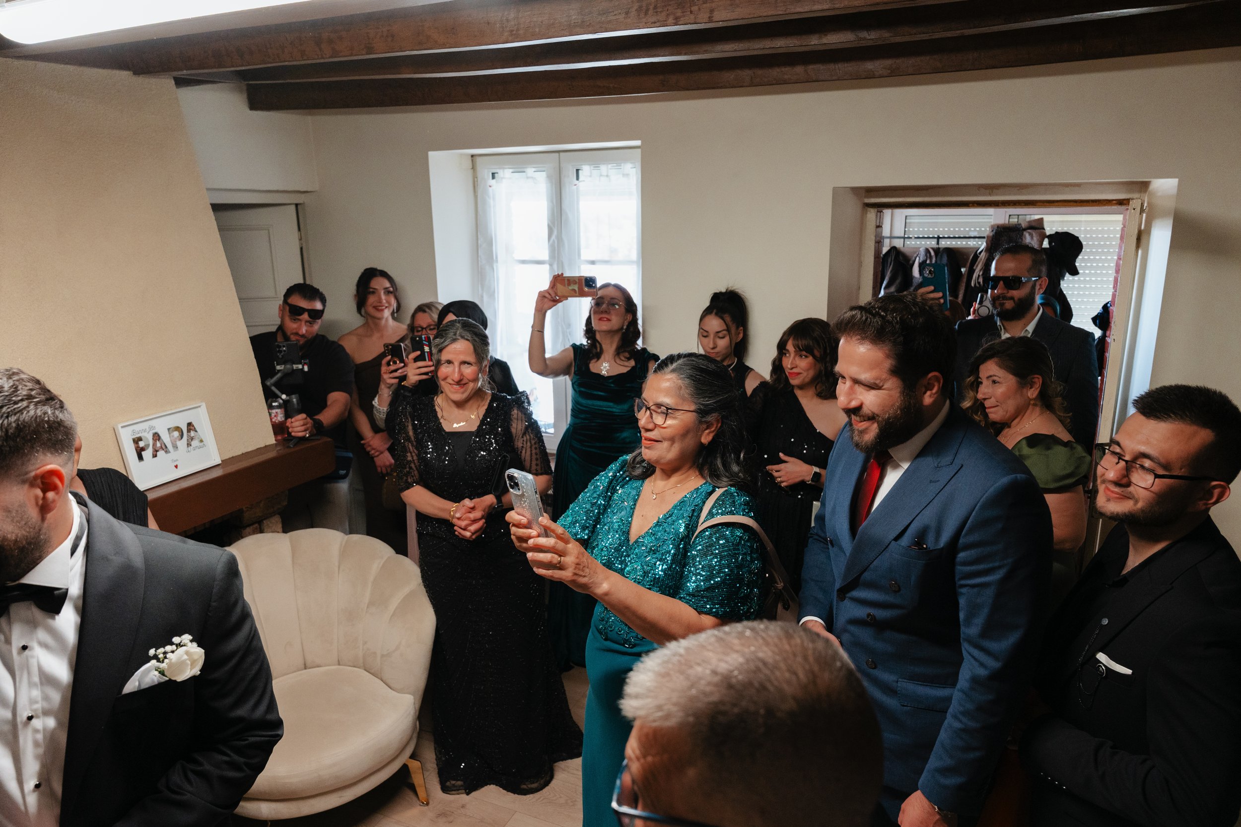Groupe de personnes habillées de façon élégante, prenant des photos et souriant lors d'une réunion ou célébration à l'intérieur d'une maison