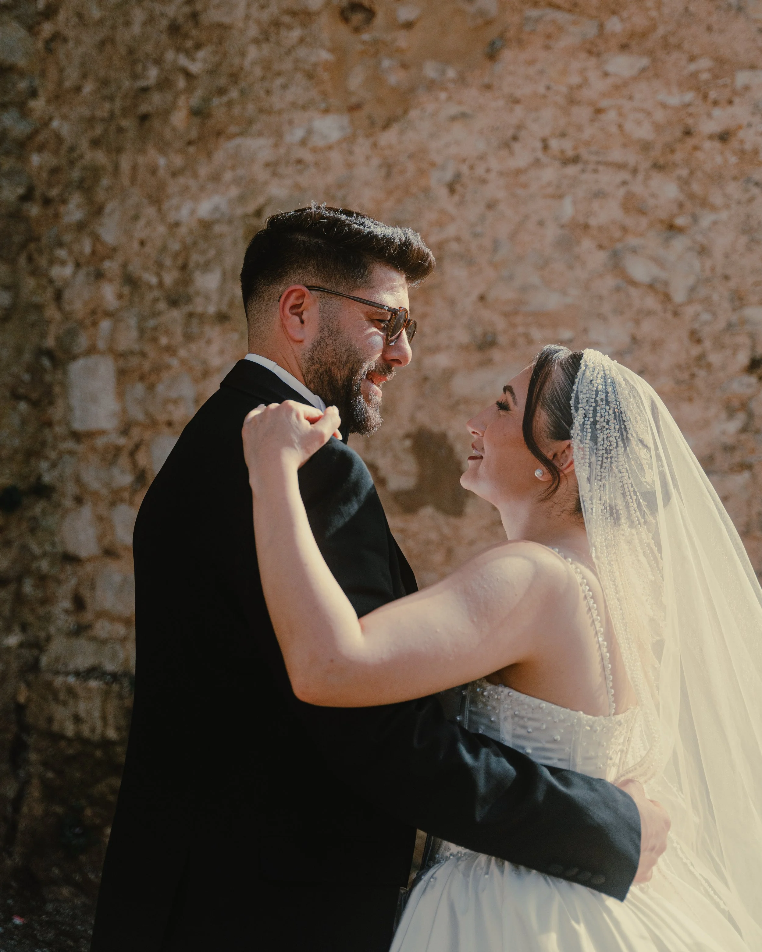 Un couple de mariés dansant lors de leur mariage, avec un mur de pierre en arrière-plan.