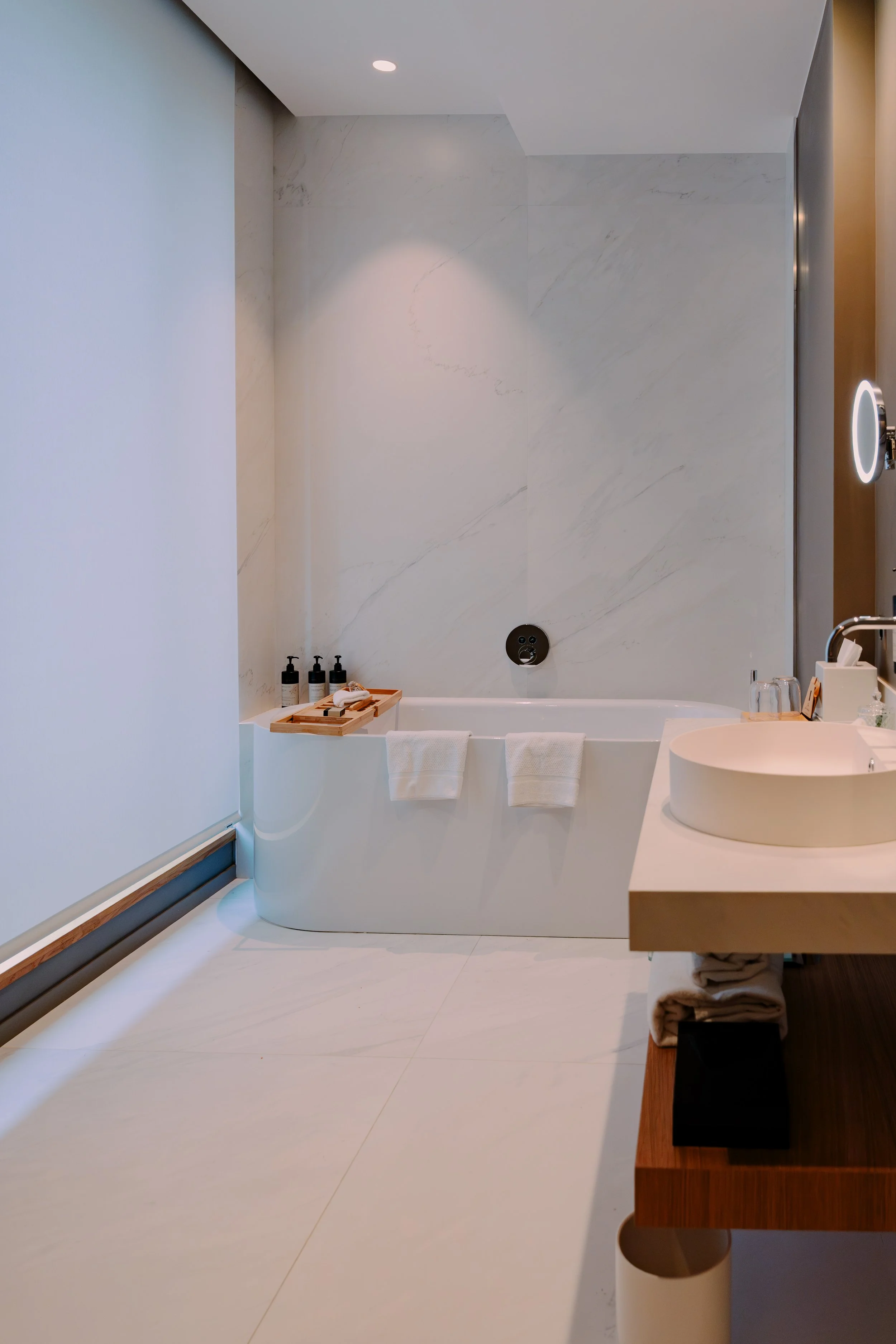 Salle de bain moderne avec baignoire, lavabo rond, miroir à LED, et accessoires de toilette en noir et blanc.