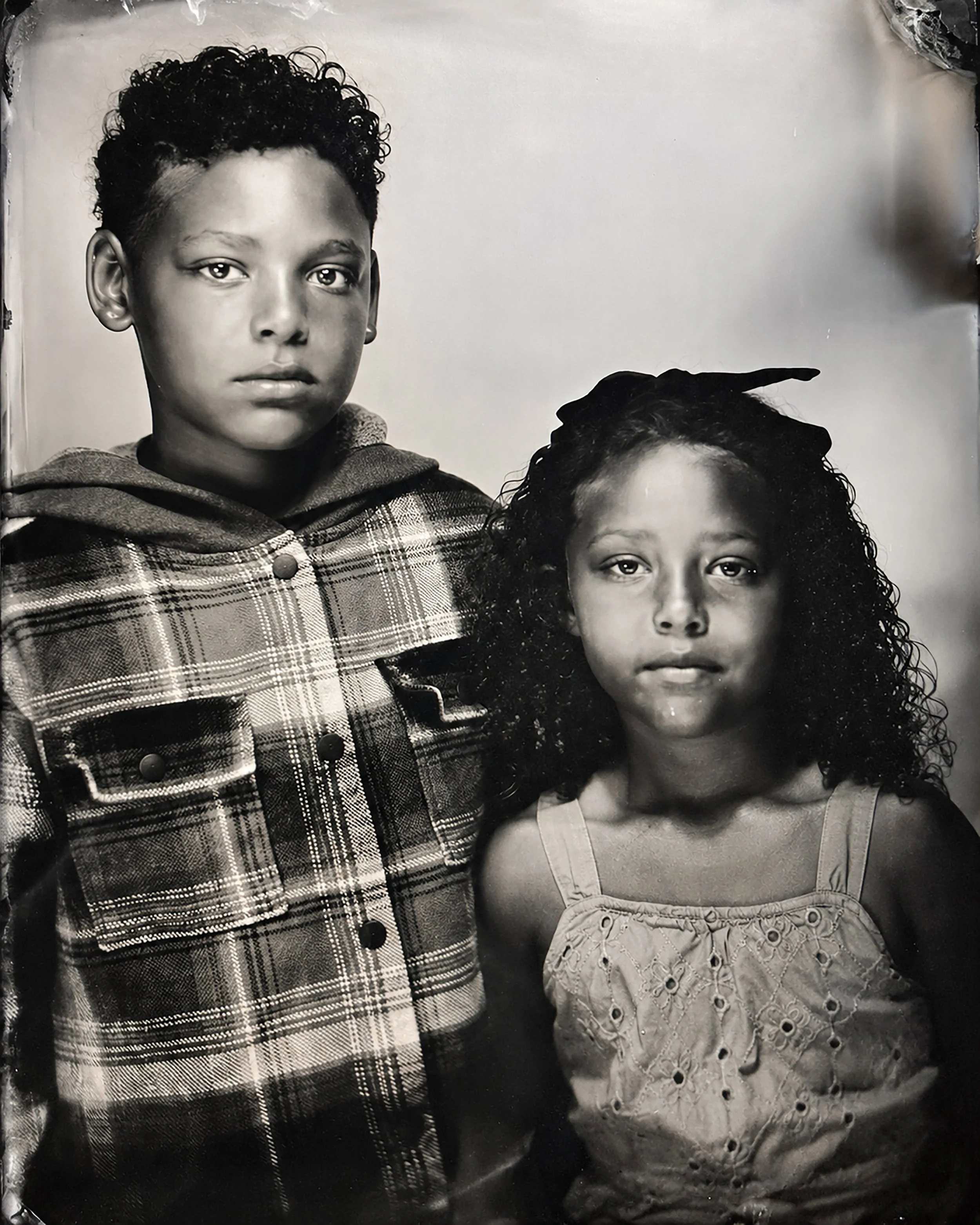 Black and white portrait of two young children, a boy and a girl, facing the camera, with the boy slightly taller and standing behind the girl.  TINTYPE PORTRAIT