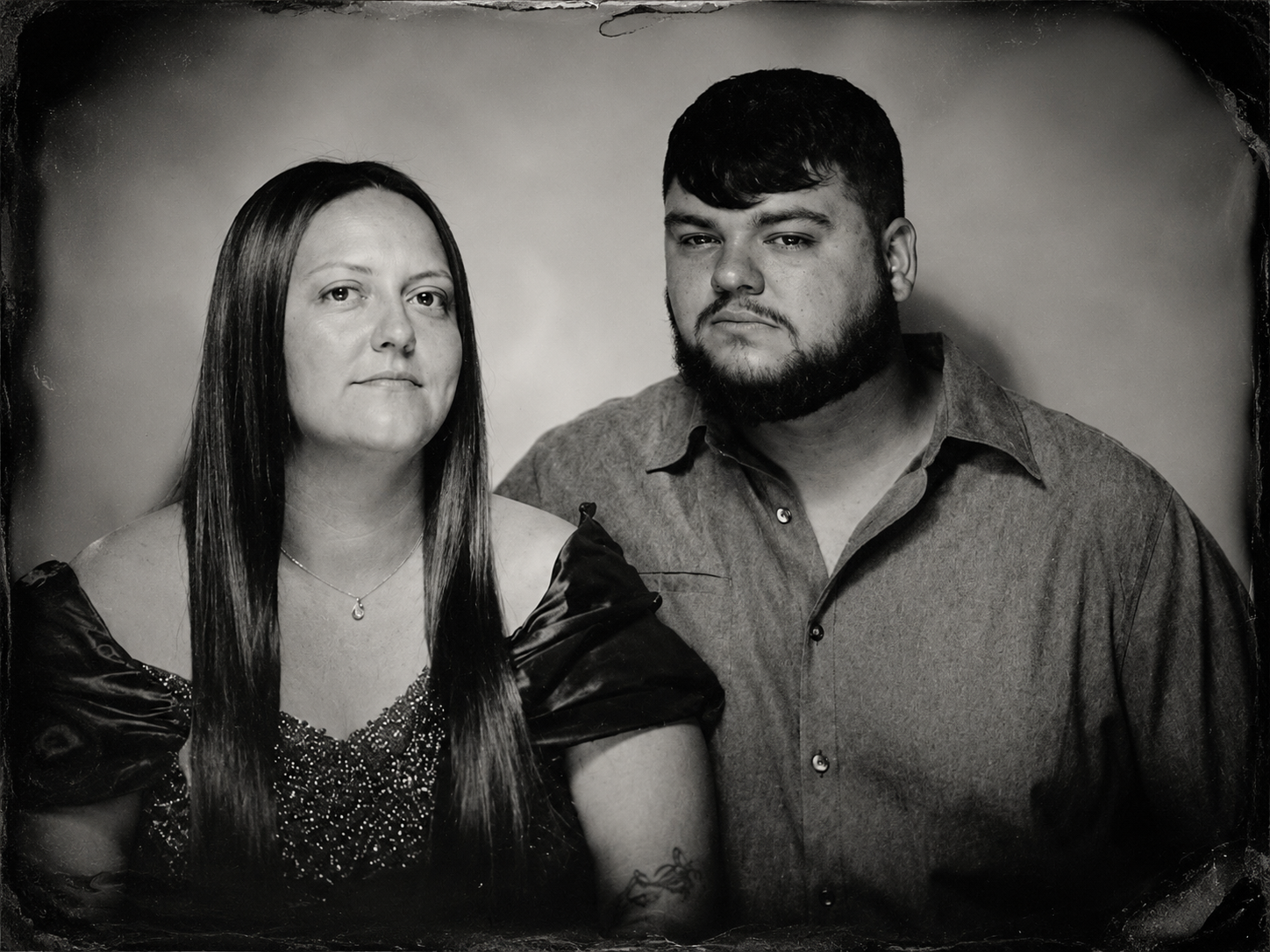 A black-and-white portrait of a woman with long straight hair and a man with a beard, both looking at the camera against a plain background.