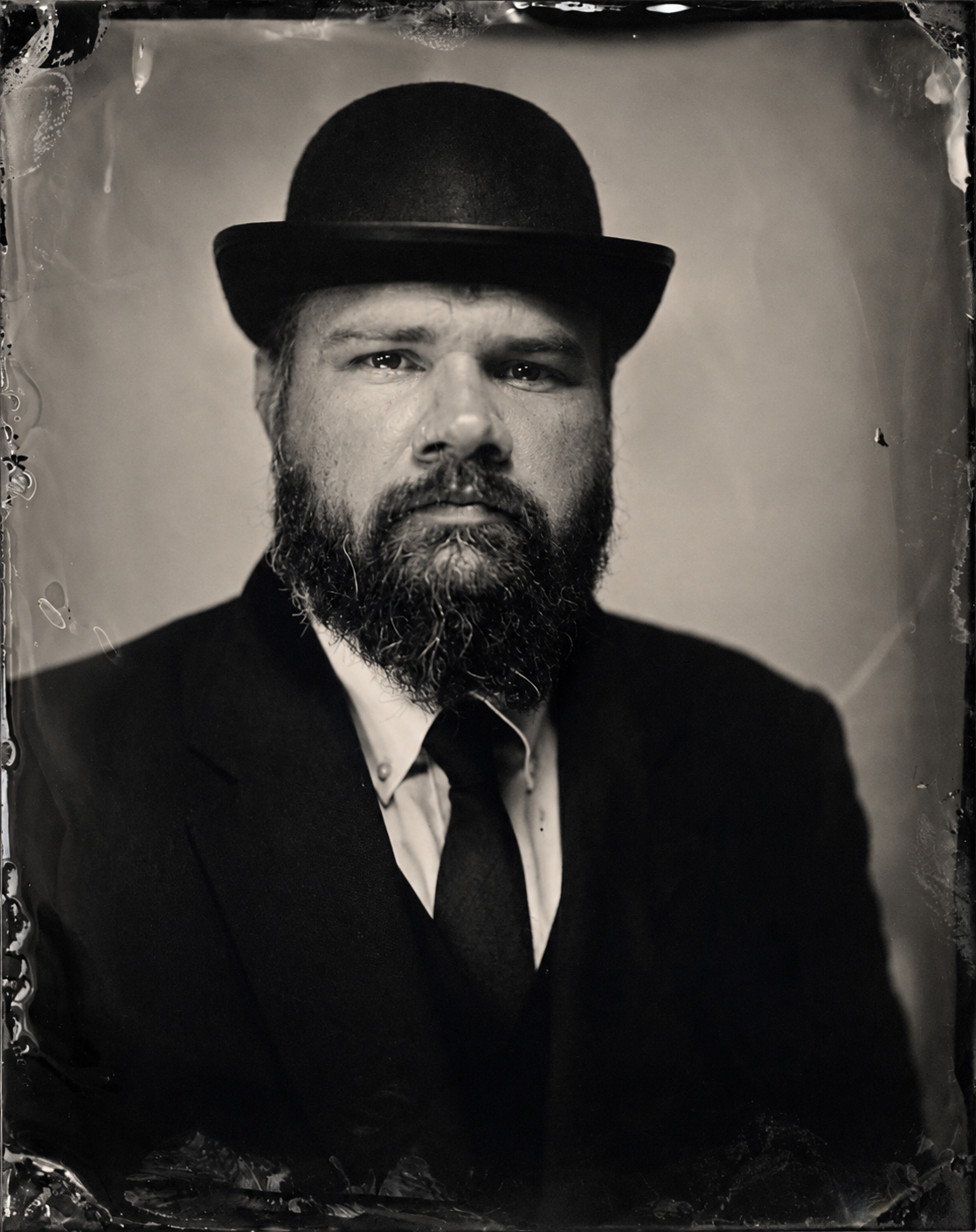Black and white portrait of a man with a beard wearing a suit, tie, and bowler hat.