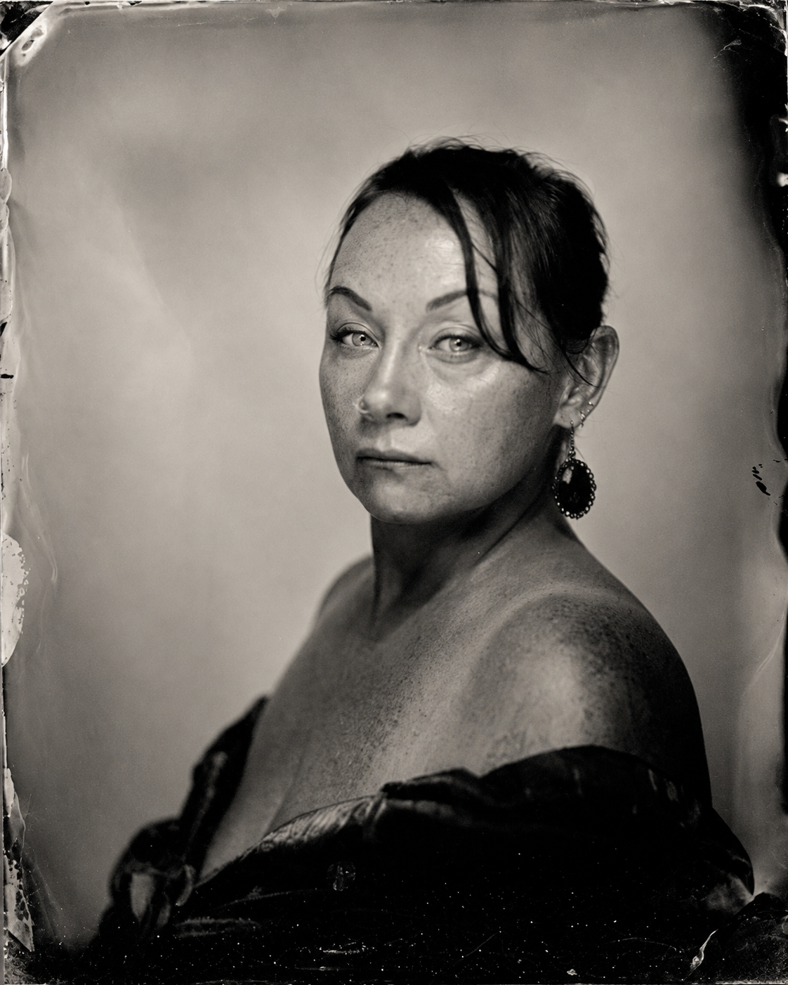 Black and white portrait of a woman with short dark hair, wearing a large earring, and a dark off-shoulder garment.