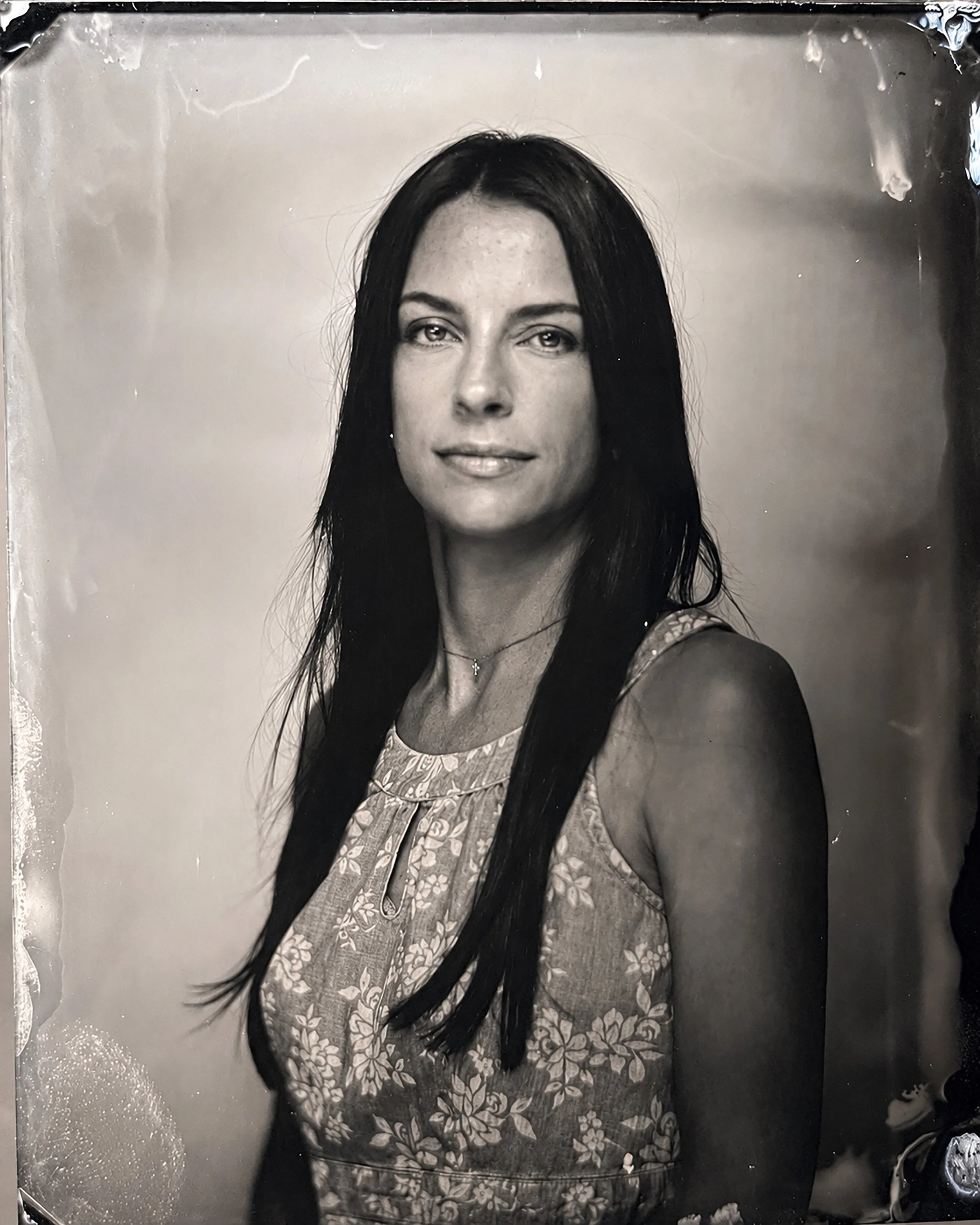 Black and white photograph of a woman with long dark hair, wearing a patterned top, smiling slightly, looking at the camera.  TINTYPE PORTRAIT