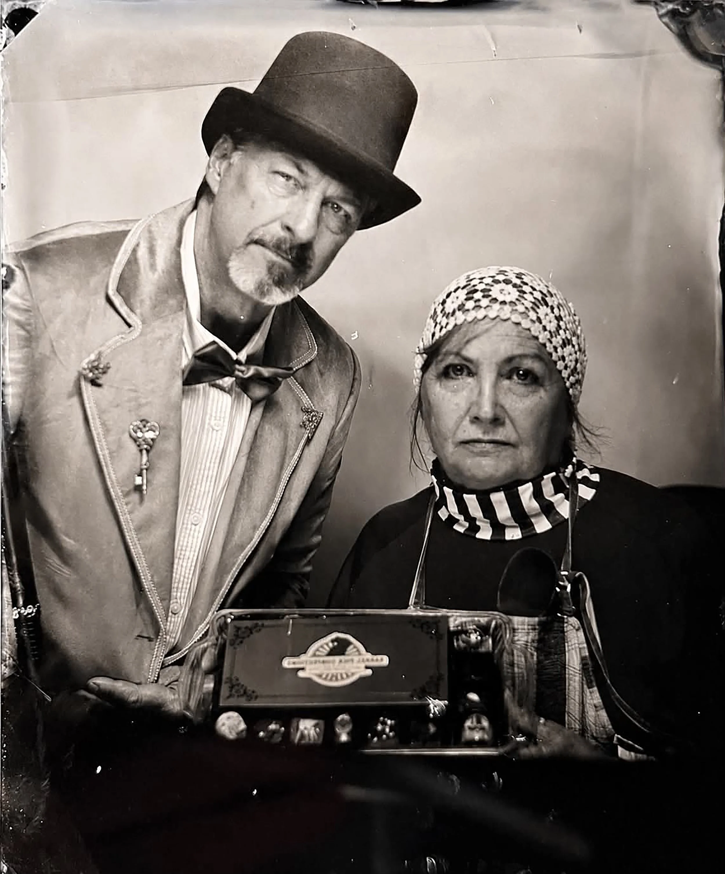 A framed black and white photo of a man and a woman. The man is wearing a tall top hat and a vintage style jacket with medals, while the woman wears a headscarf and has a serious expression.