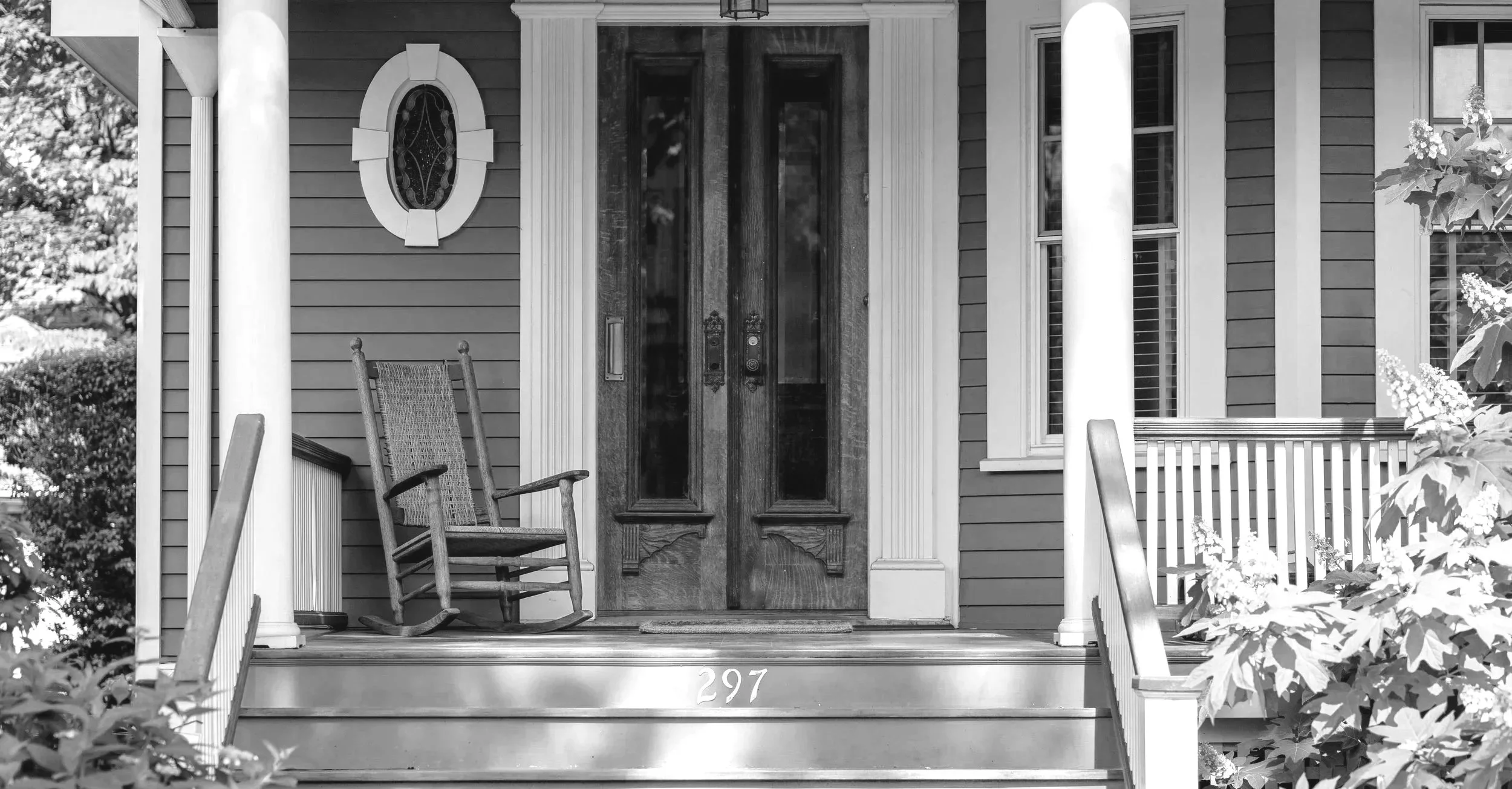 Front porch of a traditional home with wooden rocking chair and double front doors