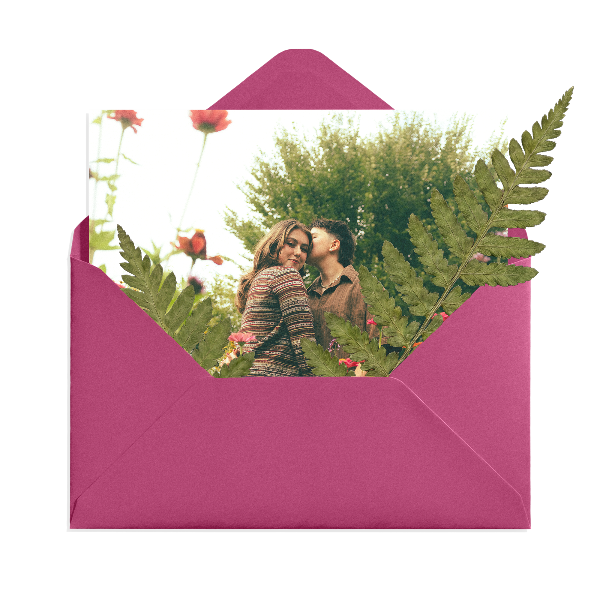 A pink gift box with a photograph of a smiling couple under a large fern leaf, set outdoors with trees and flowers in the background.