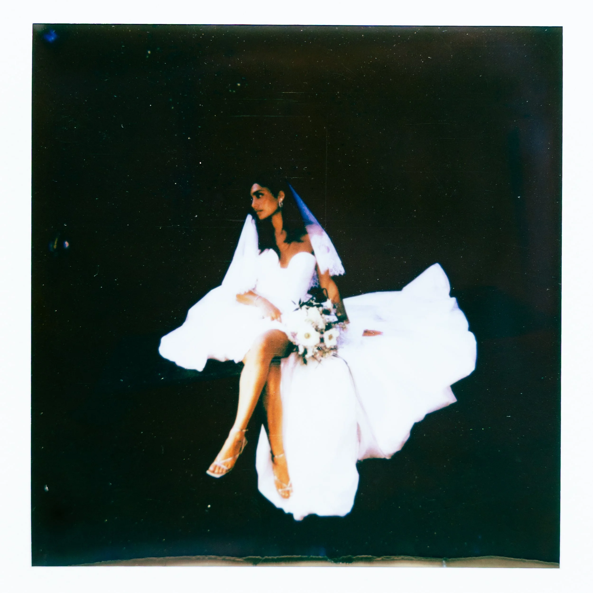 A Polaroid photo showing a woman with dark hair in a white dress, standing against a dark, starry background.