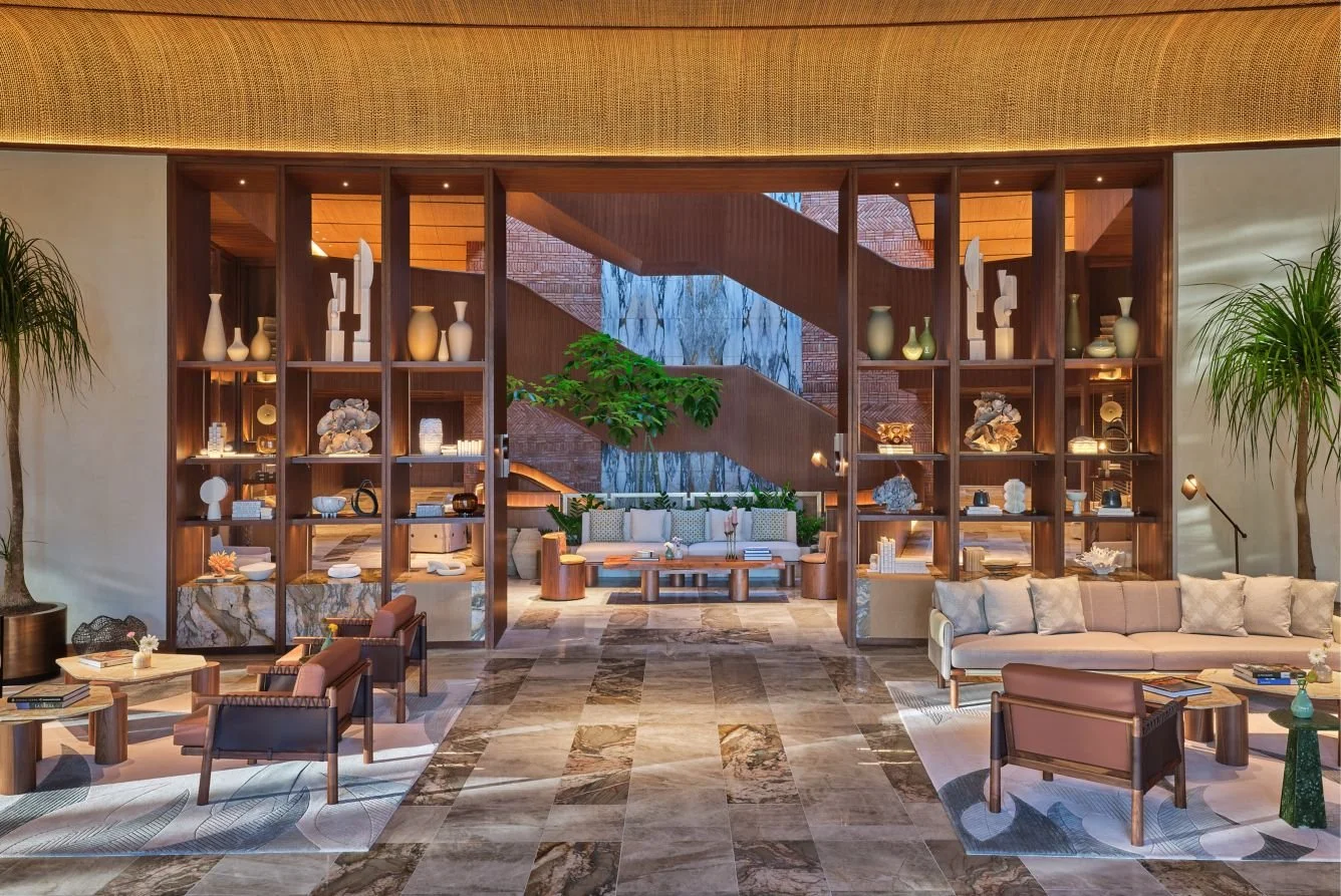 Luxury hotel lobby with modern decor, seating areas, decorative shelves, plants, and staircase in the background.