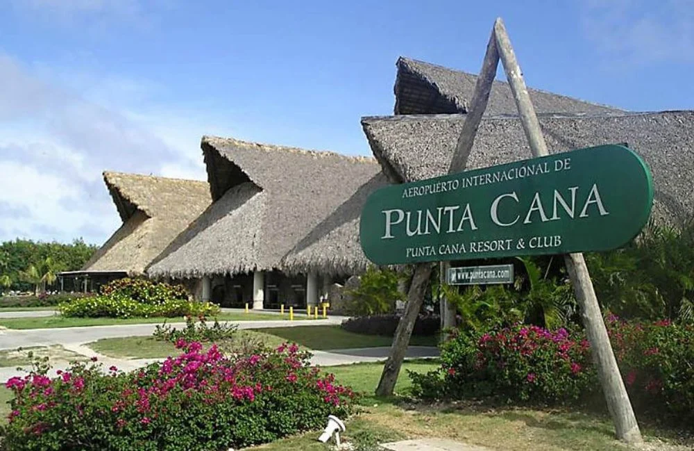 Entrance of Punta Cana International Airport and Resort, with thatched roof buildings and a large green sign.