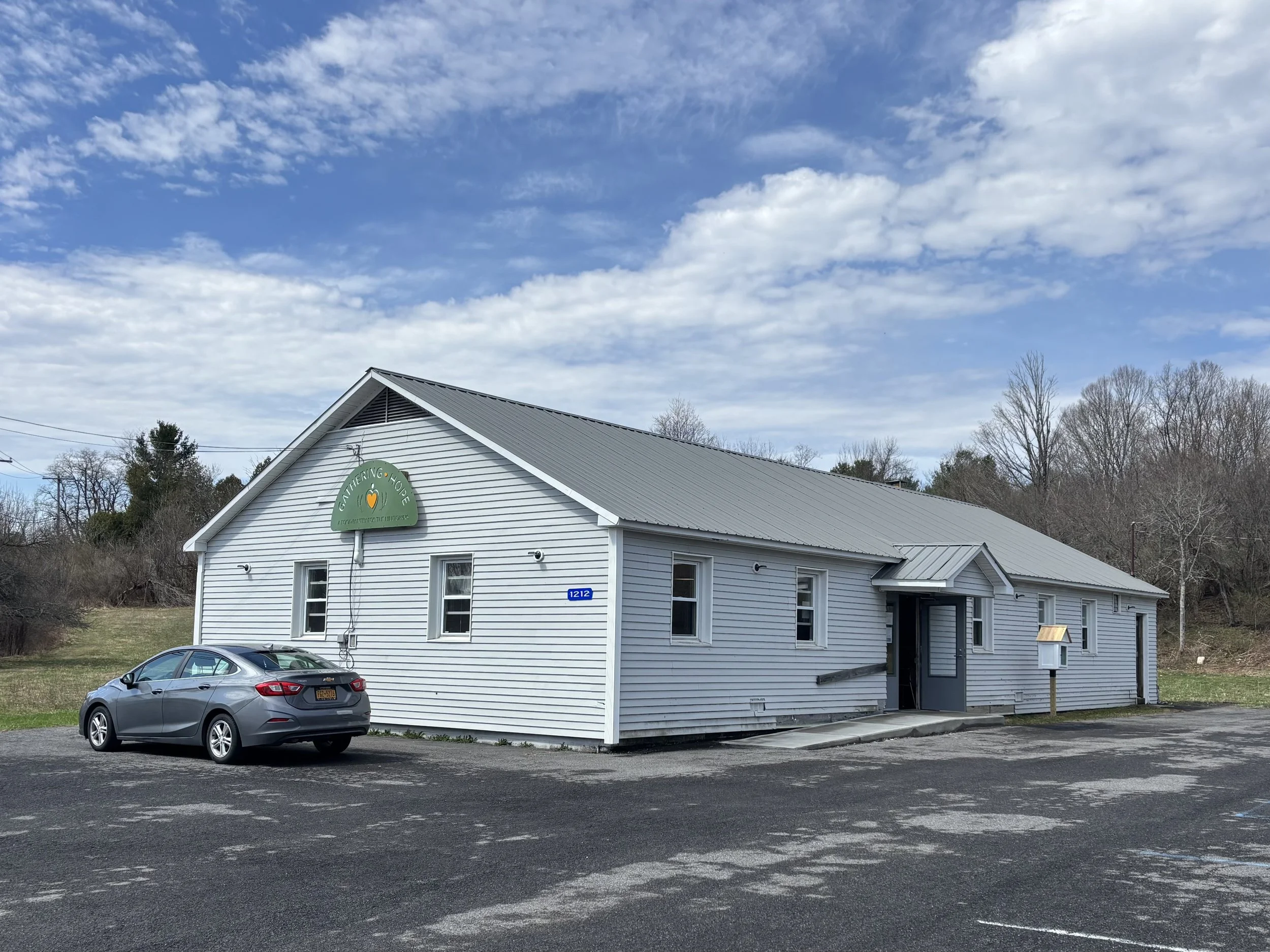 White building with a gray metal roof, and a sign that reads 'Gathering Hope Food Pantry'.