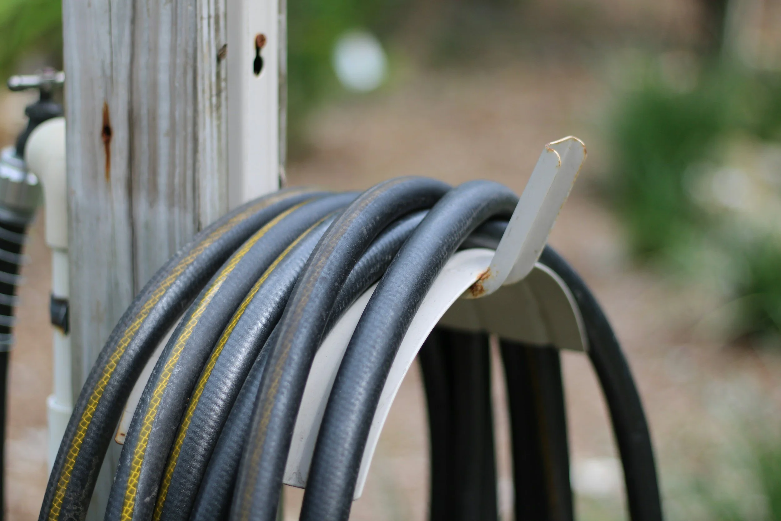 Coiled extension cords hanging on a white hook attached to a wooden post outdoors.