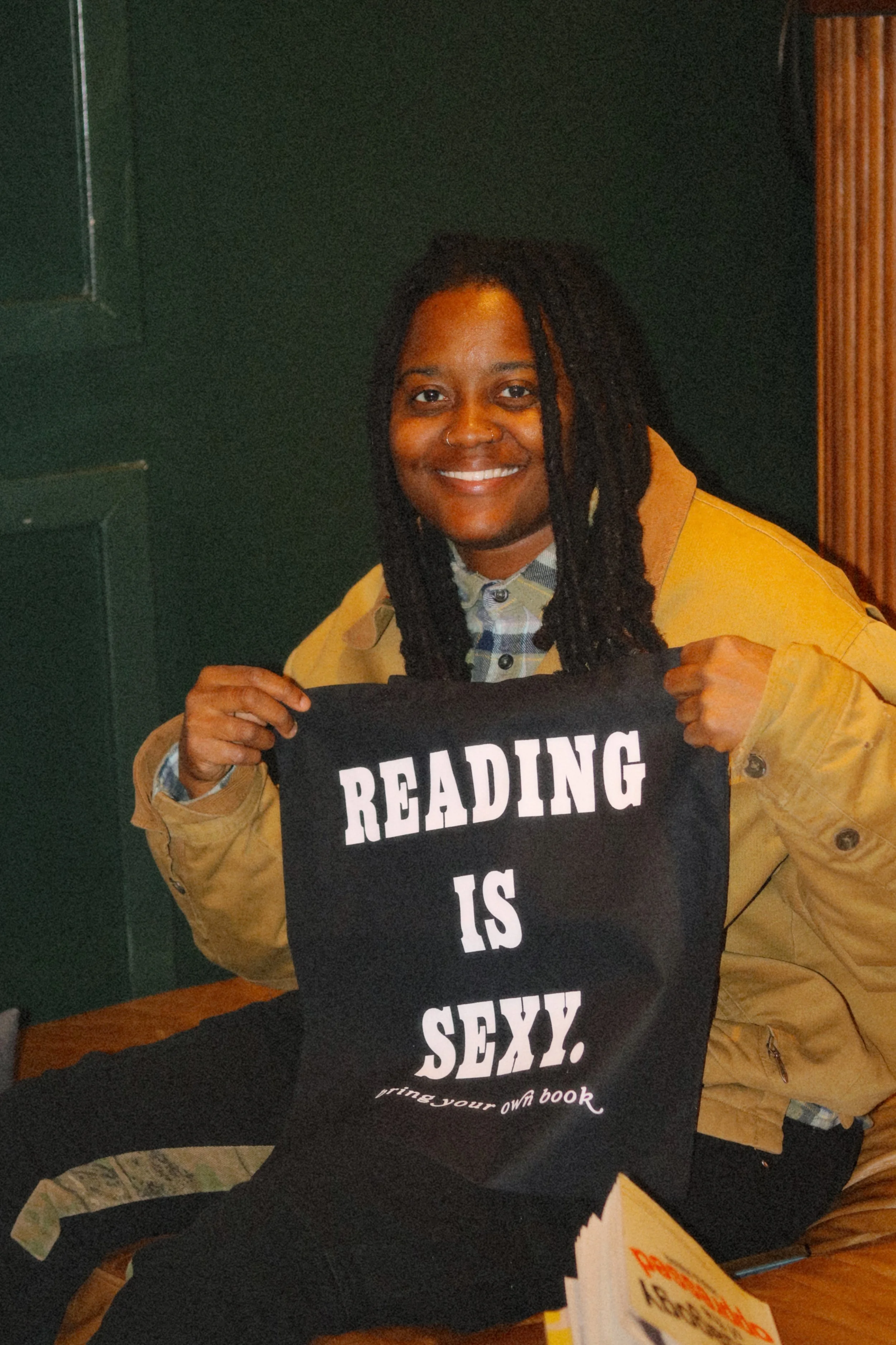 A woman holding a Reading is Sexy tote bag, a giveaway from a Bring Your Own Book event hosted at Shanklin Hall