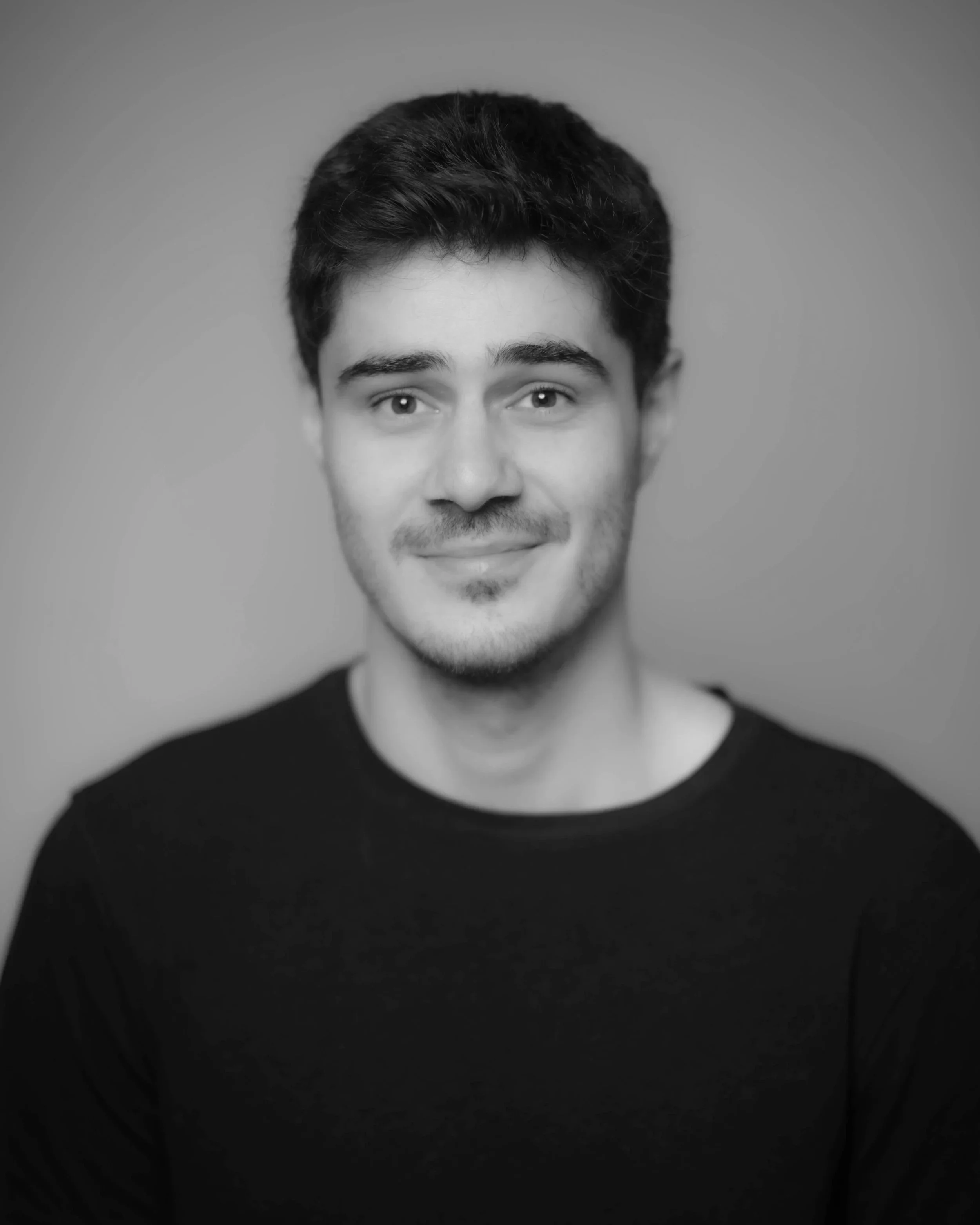 Black and white portrait of a smiling young man with short dark hair, wearing a dark shirt, against a plain background.