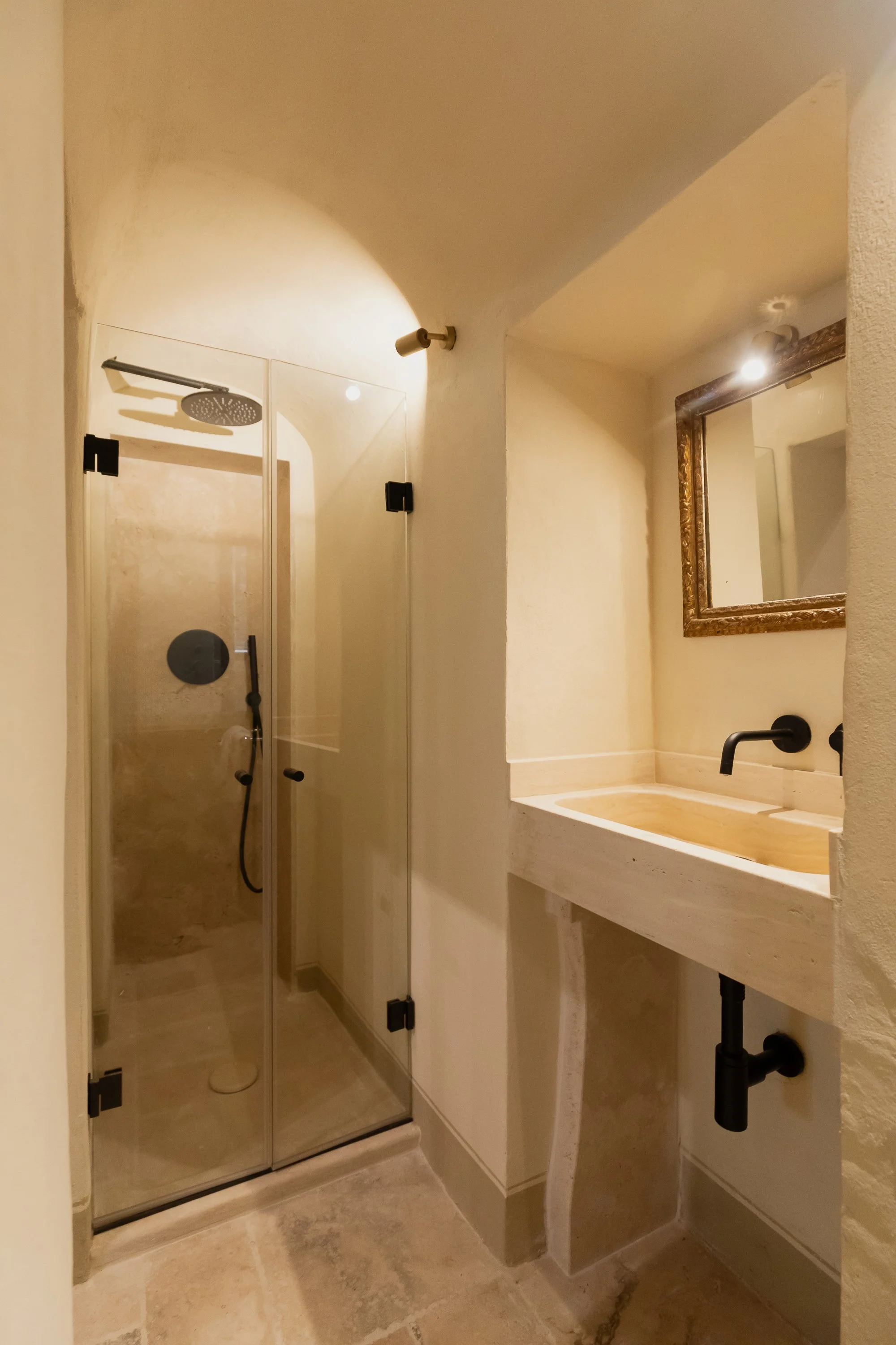 Small bathroom with a glass-enclosed shower with a rainfall showerhead, a stone sink with a black faucet, and a mirror with a decorative frame.