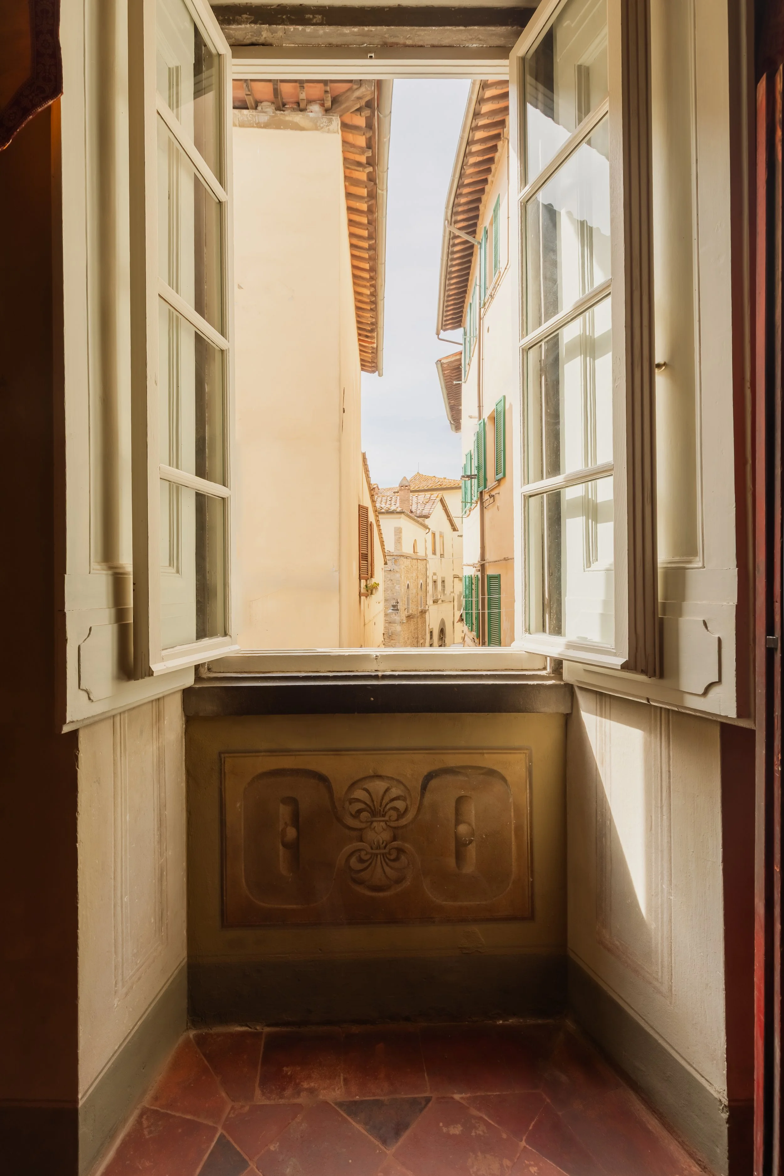 Open window overlooking a narrow European street with buildings and green window shutters.