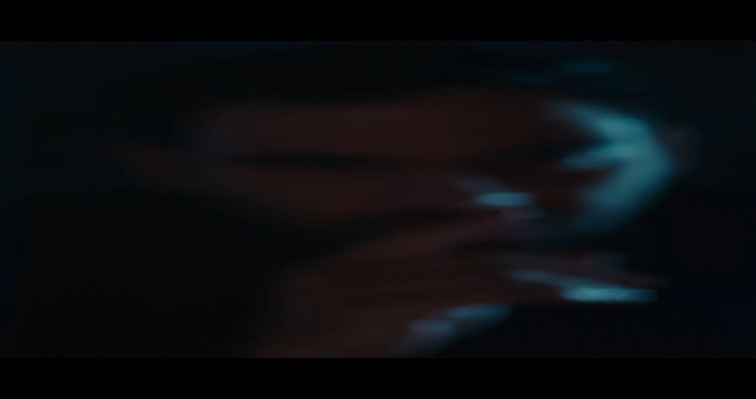 Blurred image of a person's hand holding a pen or stylus, writing or drawing on a surface in a dark setting.