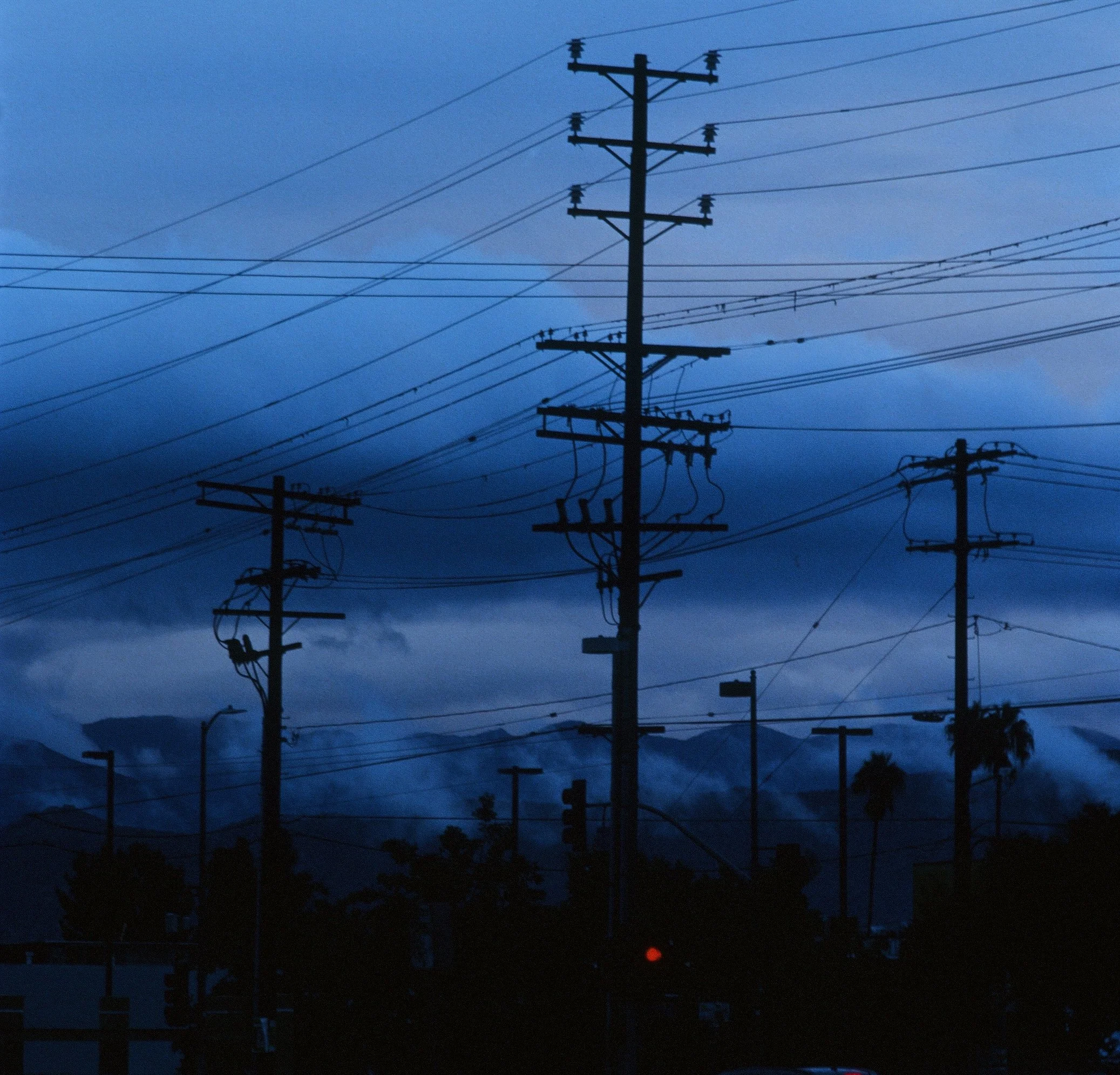 Silhouetted power lines and utility poles against a darkening sky near dusk or dawn, with some clouds and distant mountains or hills in the background.