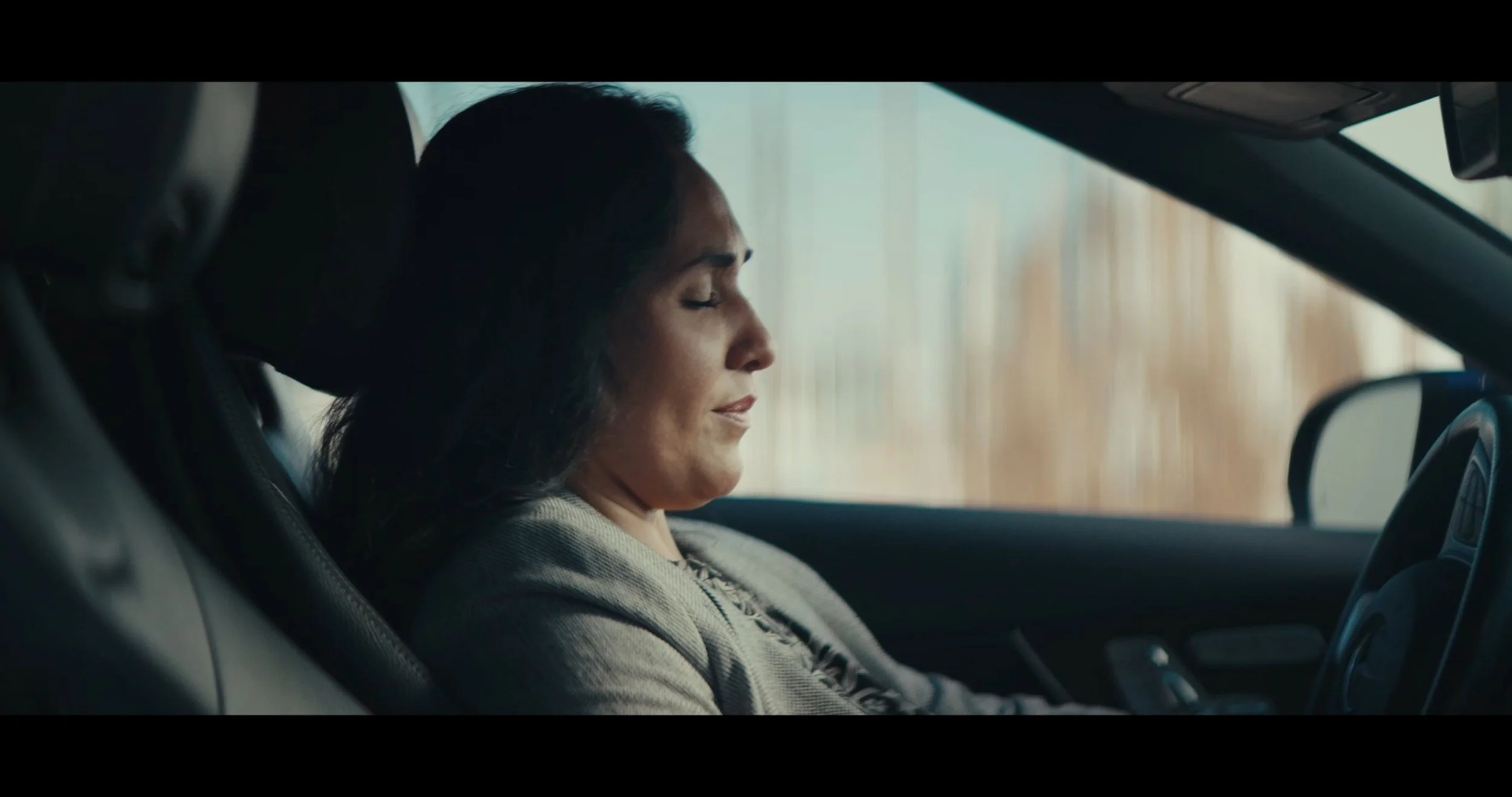 Woman with closed eyes and relaxed expression sitting in the passenger seat of a car.