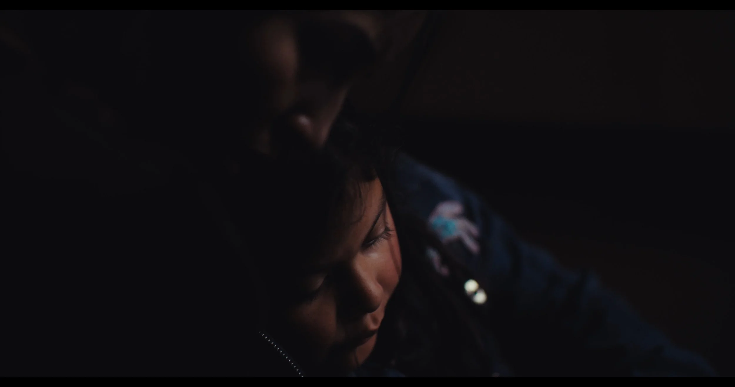 A close-up image showing a woman with long eyelashes and a man with glasses, both in a dark environment.
