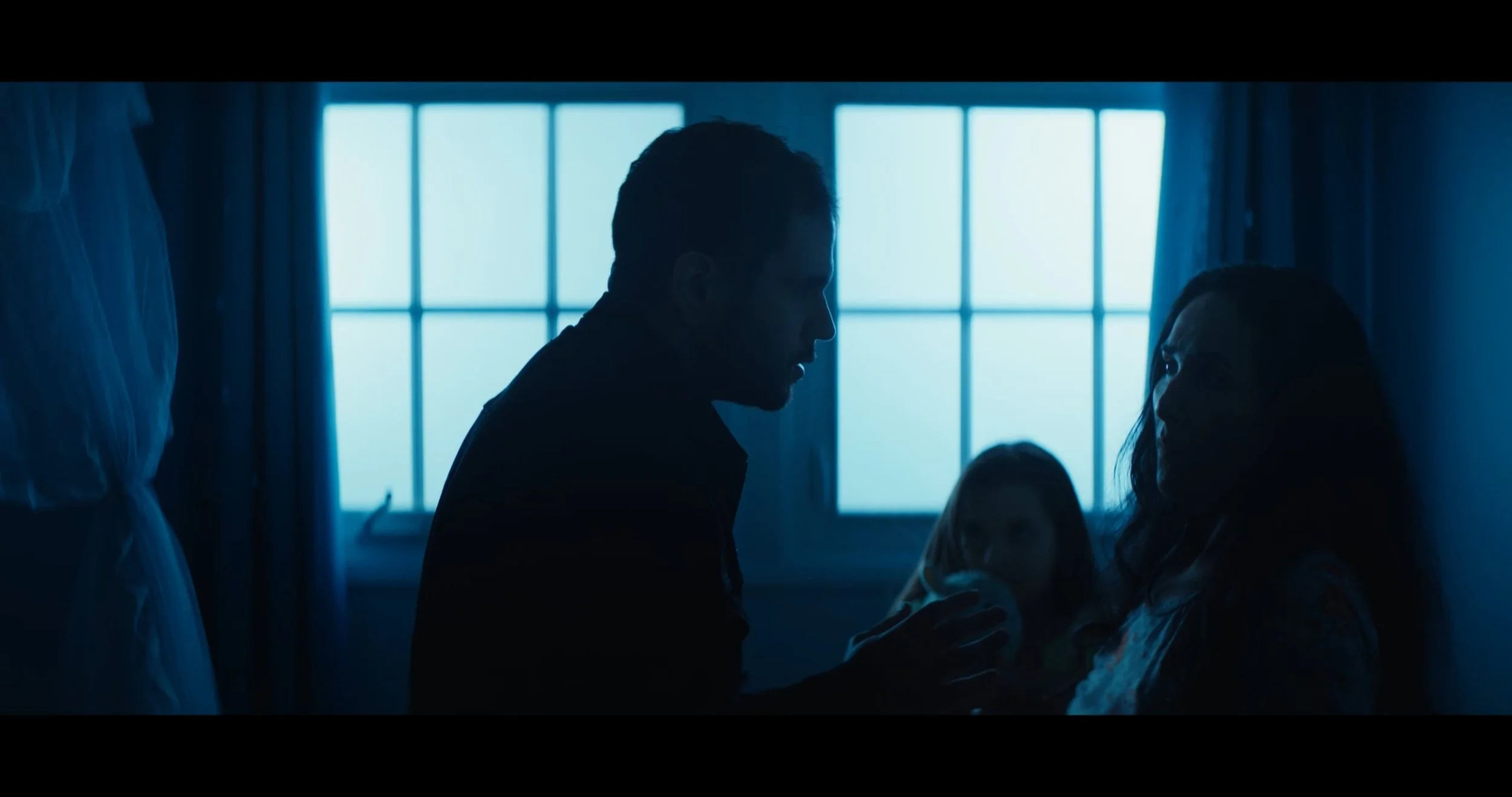 A silhouette of a man leaning towards a woman sitting in a hospital bed, with a large window in the background illuminating the scene.