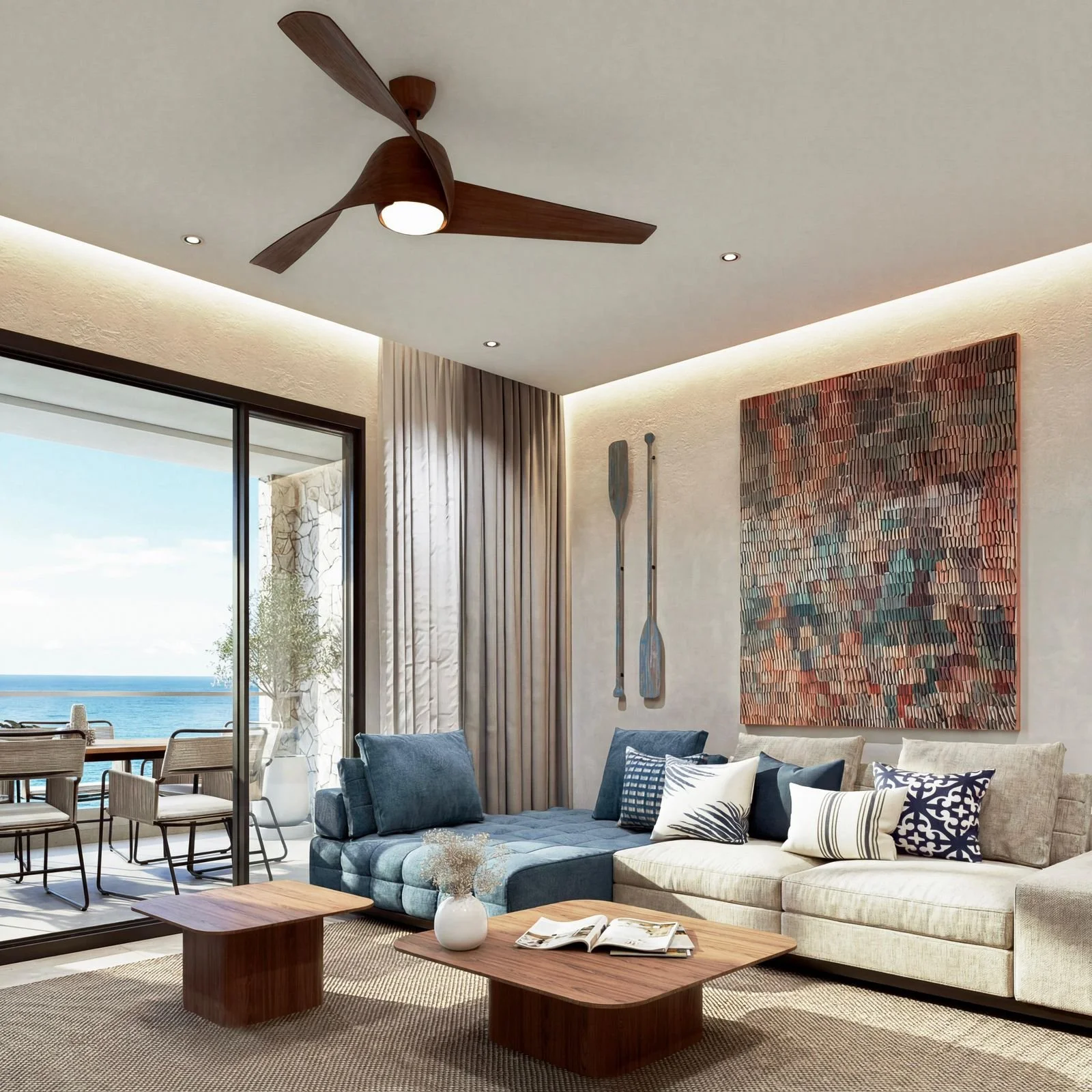 Living room with a large white sectional sofa adorned with various black and white cushions, a wooden coffee table with an open magazine and a white vase, a textured wall art piece, potted plant outside a glass sliding door, and a view of the ocean.