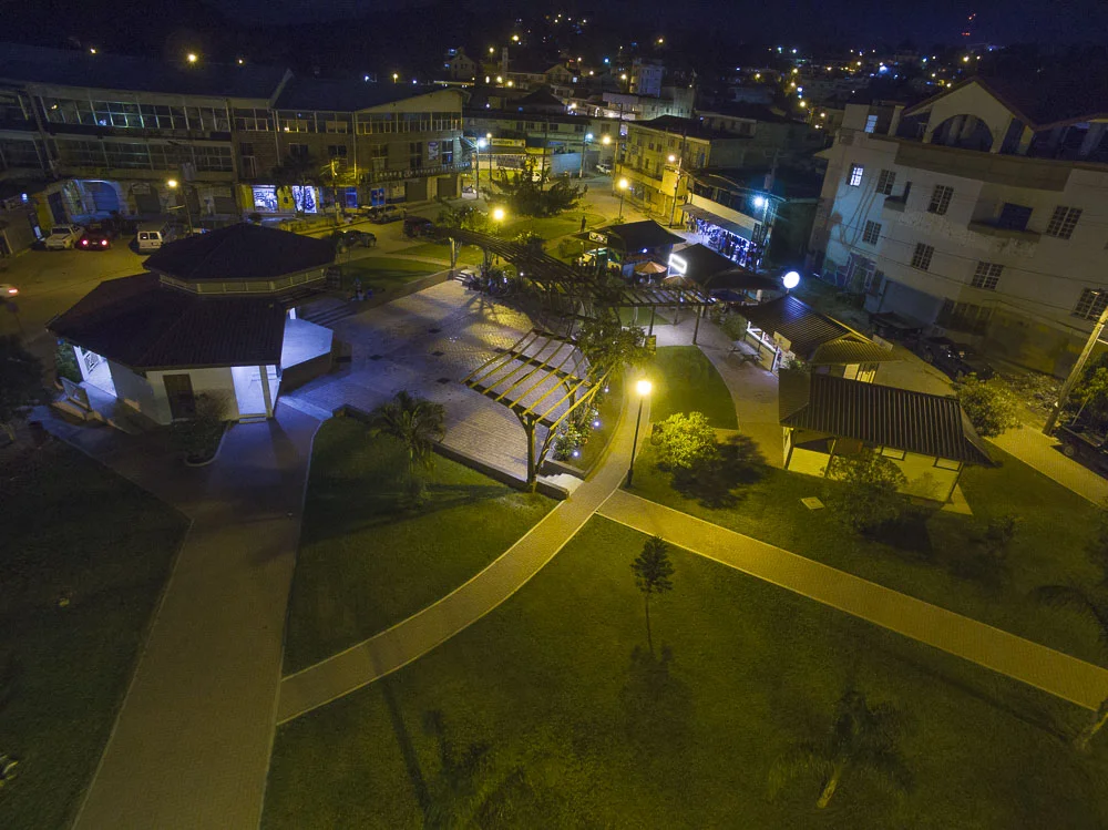 Nighttime view of a small park with walkways, a pavilion, and surrounding buildings, illuminated by street lamps.